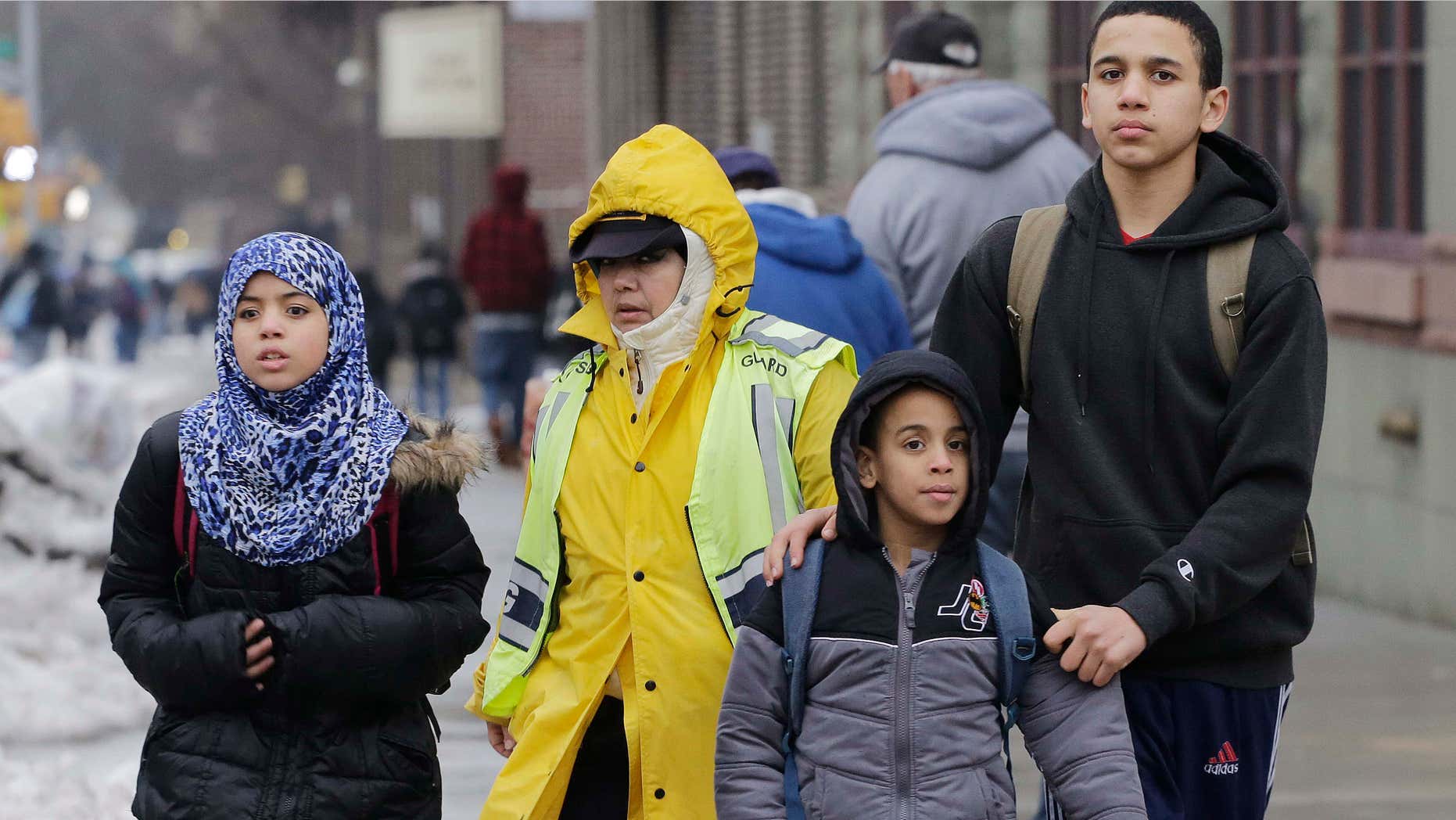 A crossing guard assists three Muslim school children at the end of a school day.