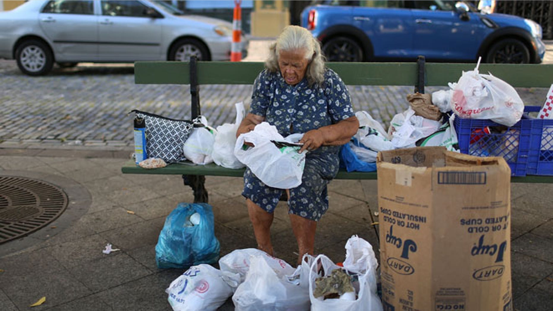 SAN JUAN, PUERTO RICO - JUNE 30: A woman sorts through her belongings on a park bench a day after the speech Puerto Rican Governor Alejandro Garcia Padilla gave regarding the government's $72 billion debt on June 30, 2015 in San Juan, Puerto Rico. The Governor said in his speech that the people will have to sacrifice and share in the responsibilities for pulling the island out of debt. (Photo by Joe Raedle/Getty Images)