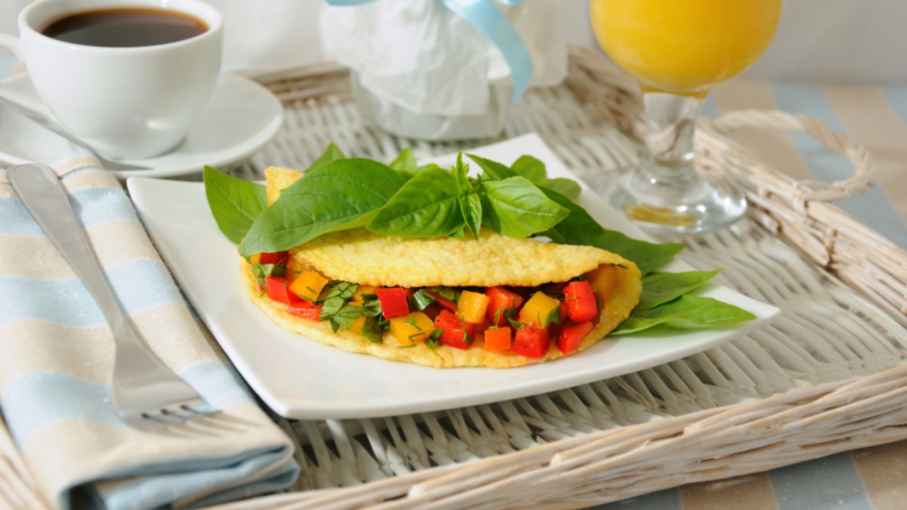 An omelet stuffed with vegetables with basil, orange juice on a tray