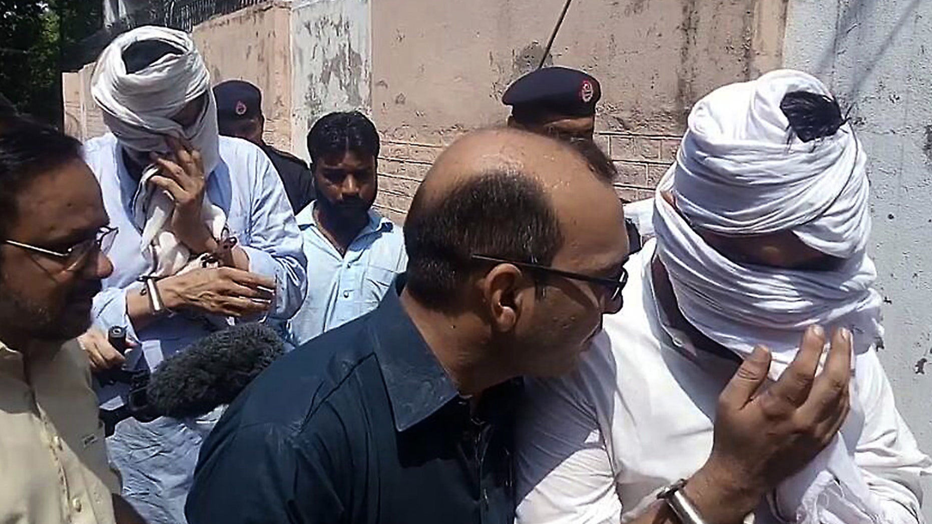 In this Monday, Sept. 5, 2016 photo, Pakistani police officers escort the detained father, second left face covered, and husband, right face covered, of slain British women Samia Shahid, to appear in court in Jhelum, in eastern Pakistan, Wednesday, Sept. 7, 2016.