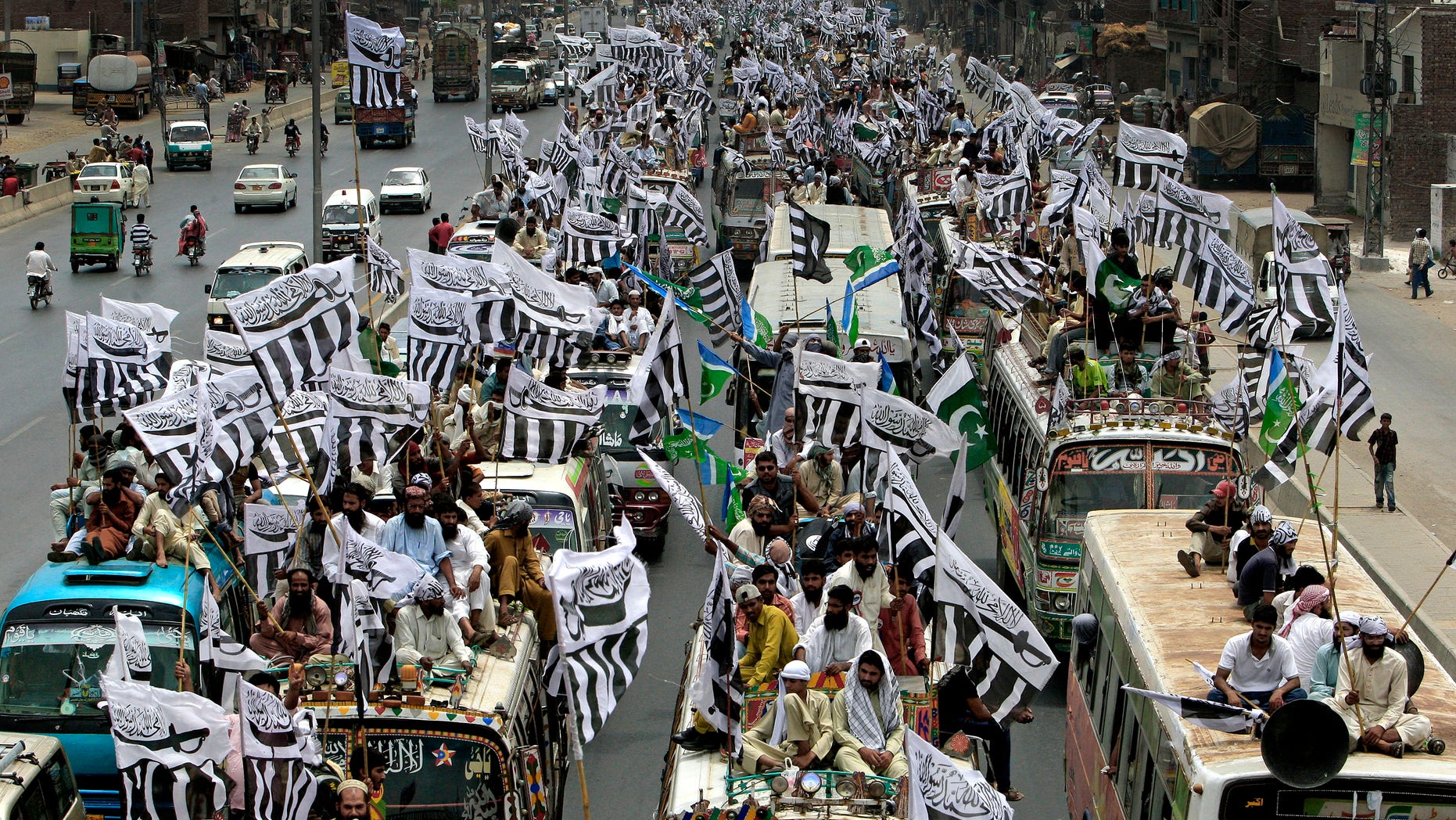 July 8, 2012: Supporters of the Defense Council of Pakistan sit on the top of vehicles with party flags as they take part in a rally, in Lahore, Pakistan.