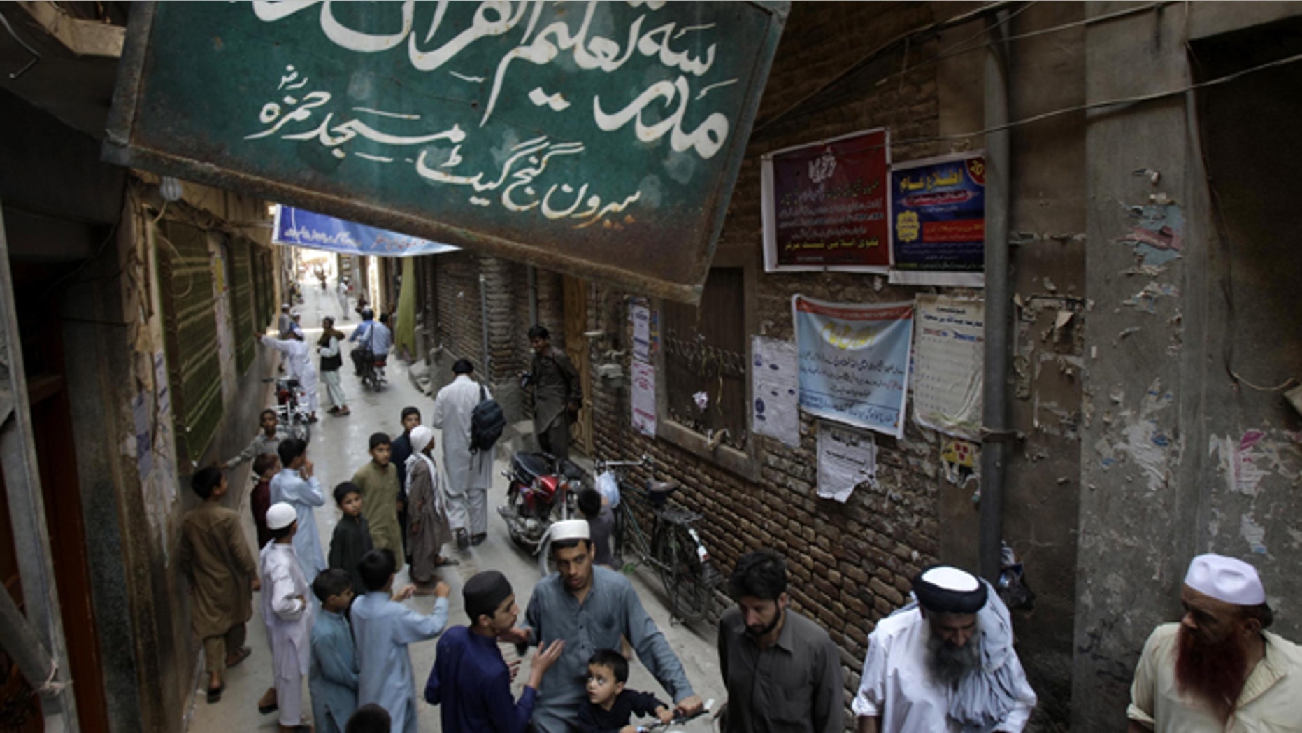 Aug. 21, 2013: People gather outside the Jamia Taleem-Ul-Quran-Wal-Hadith Madrassa, in Peshawar, Pakistan. The United States has placed unprecedented sanctions on an Islamic school in northwest Pakistan for allegedly training and financing fighters from Al Qaeda and other militant groups. Board on top reads "school for Koran and Hadith studies."