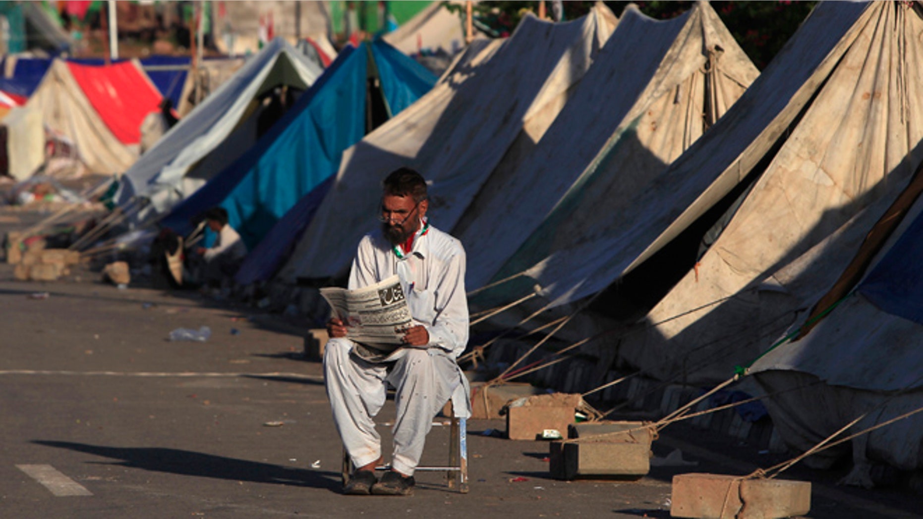 Sept. 7: An anti-government protester reads a newspaper as he sits outside makeshift tents, set up in front of the Parliament House during the Revolution March in Islamabad.