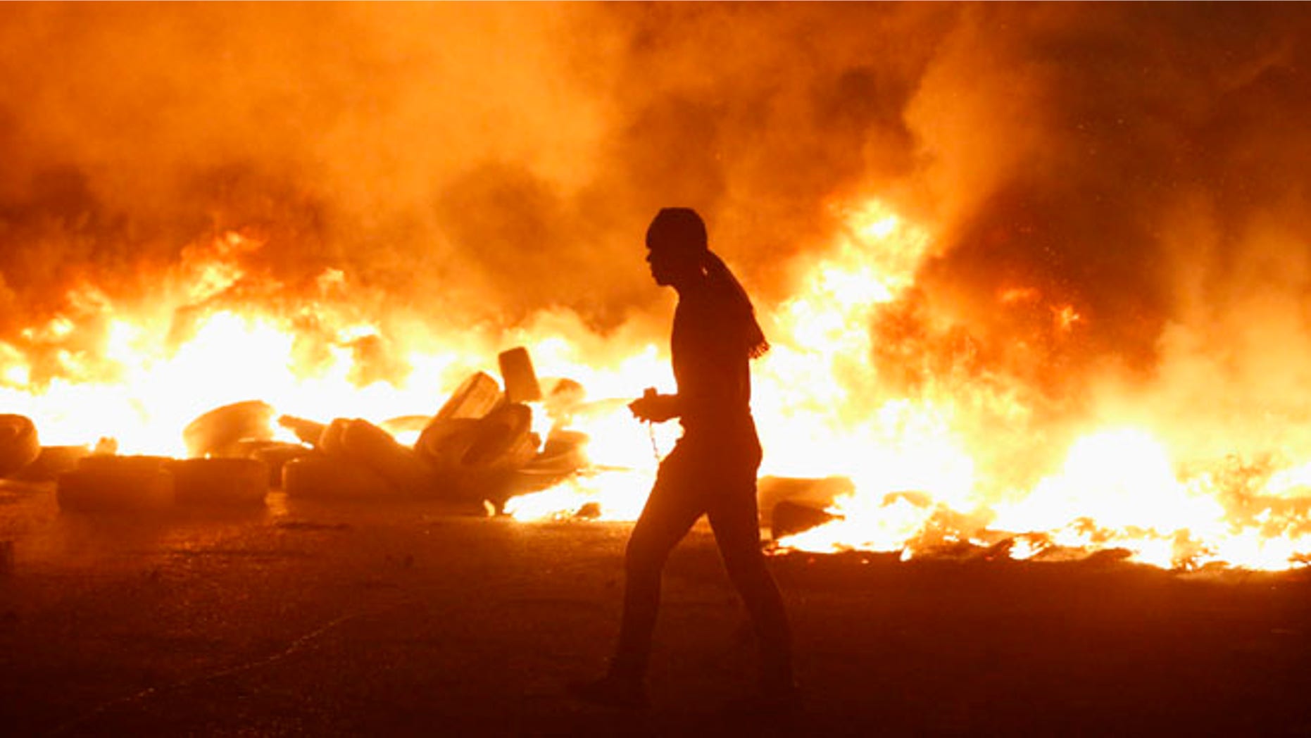 July 24, 2014: A Palestinian protester walks next to burning tyres during clashes with Israeli troops, at a protest against Israeli offensive in Gaza, at Qalandia checkpoint near the West Bank city of Ramallah.