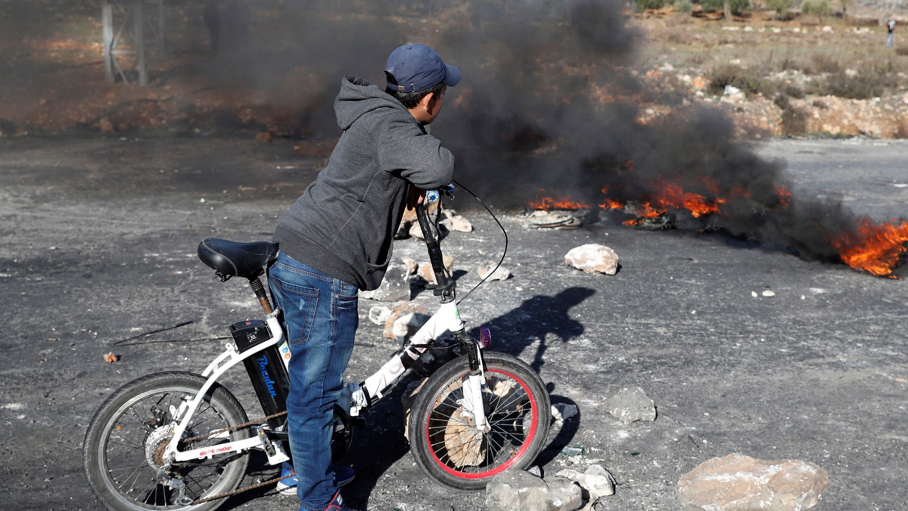 A boy stands in front of a burning barricade during a protest against U.S. President Donald Trump's decision to recognize Jerusalem as the capital of Israel, near the Jewish settlement of Beit El, near the West Bank city of Ramallah December 17, 2017.
