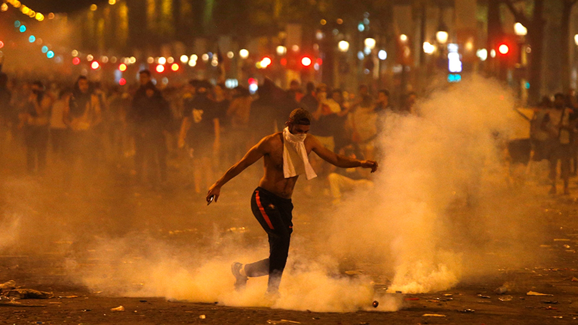 A man kicks a tear gas canister thrown by riot police during clashes on the Champs Elysees avenue where soccer fans were celebrating France's World Cup victory over Croatia.