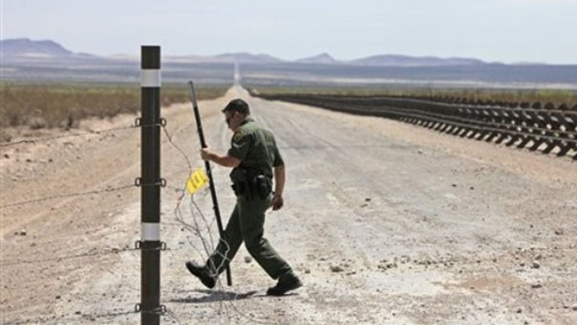 In this Aug. 6, 2009, photo, a U.S. Border Patrol agent opens a barbed wire fence leading to a road lined with vehicle barriers marking the U.S-Mexico border near Hermanas, N.M. (AP Photo)