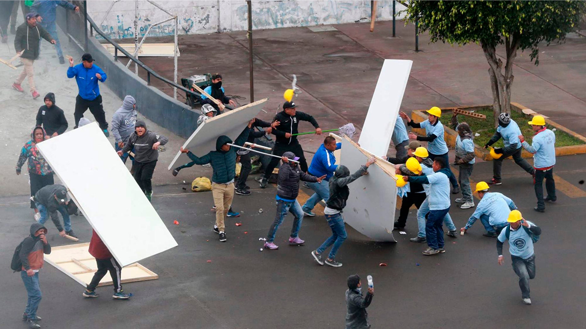 In this photo provided by the Andina government news agency, Alianza Lima club soccer fans, left, fight with members of an evangelical church, yellow helmets at right, outside the soccer club's stadium in Lima, Peru.
