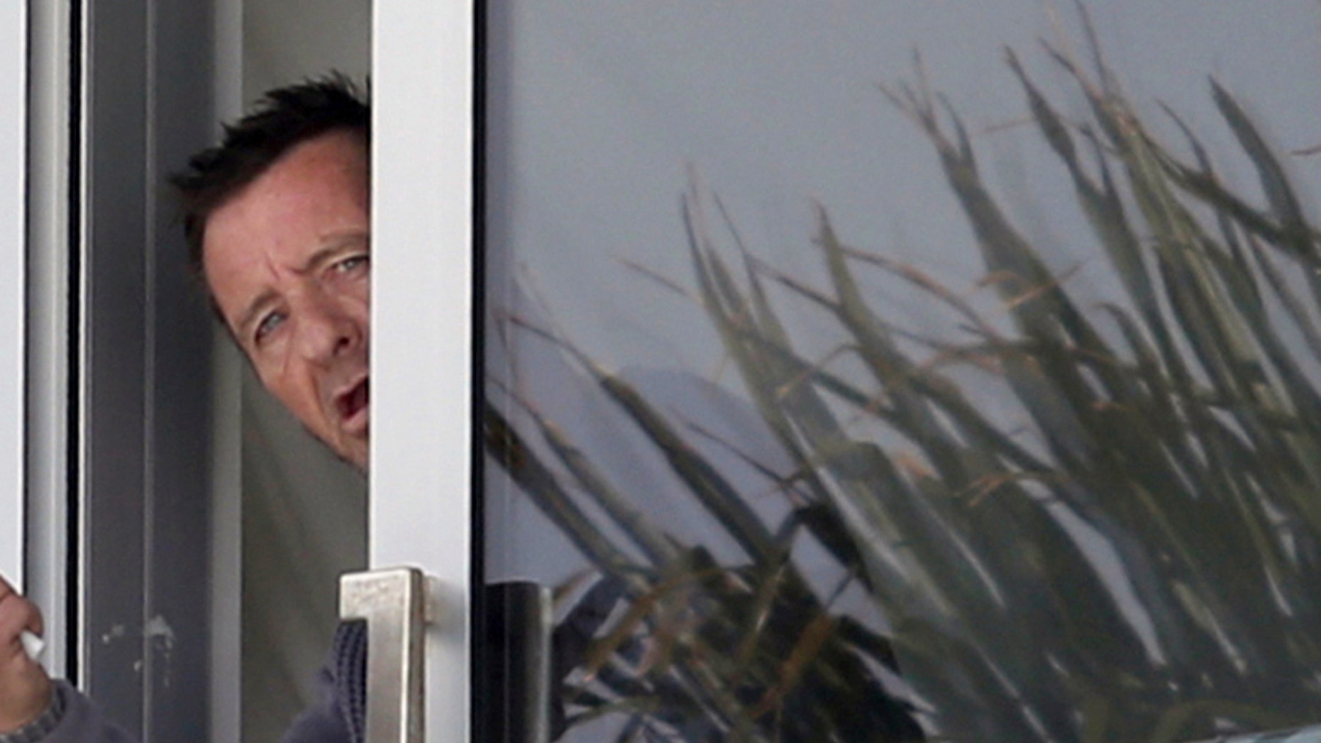 Nov. 6, 2014 file photo, Phil Rudd, drummer for the rock band AC/DC, gestures from a window at his house in Tauranga, New Zealand.