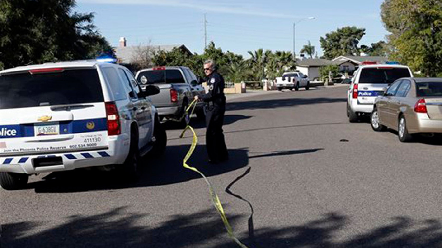 A police officer puts up some tape at the scene of a fatal house fire and shooting Tuesday, Feb. 23, 2016, in Phoenix. Officers dodged bullets fired by the shooter and donned breathing gear to enter the burning home to help the victims. (AP Photo/Morry Gash)