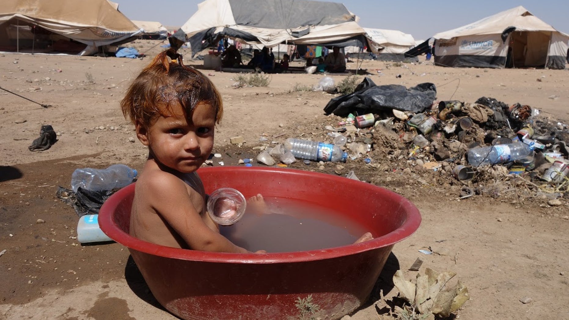 August, 2017: A child in a makeshift, polluted bath at Arisha camp in Hassakeh governorate, Syria. Around 6000 people are accommodated in the camp in very dire conditions, with no clean water, no medical services and no toilets. It was established in June 2017, and the area used to serve as an oil refinery, hence toxic waste could be found on site.
