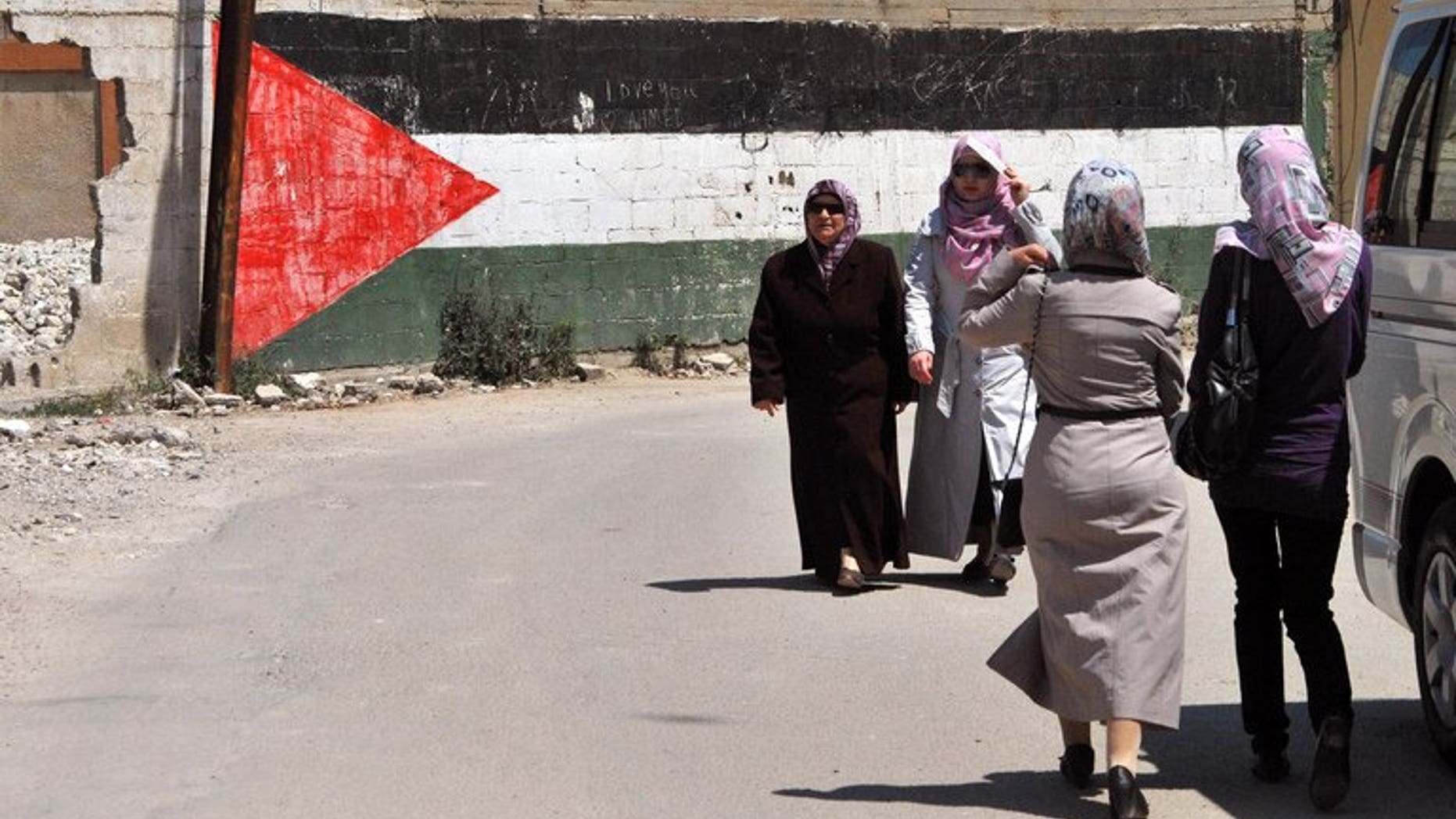 Women walk past a giant Palestinian flag painted on a wall at a camp for Palestinian refugees in Homs, Syria on May 22, 2013. The conflict in Syria has displaced more than two-thirds of Palestinian refugees living in the country, the UN Relief and Works Agency for Palestine refugees said