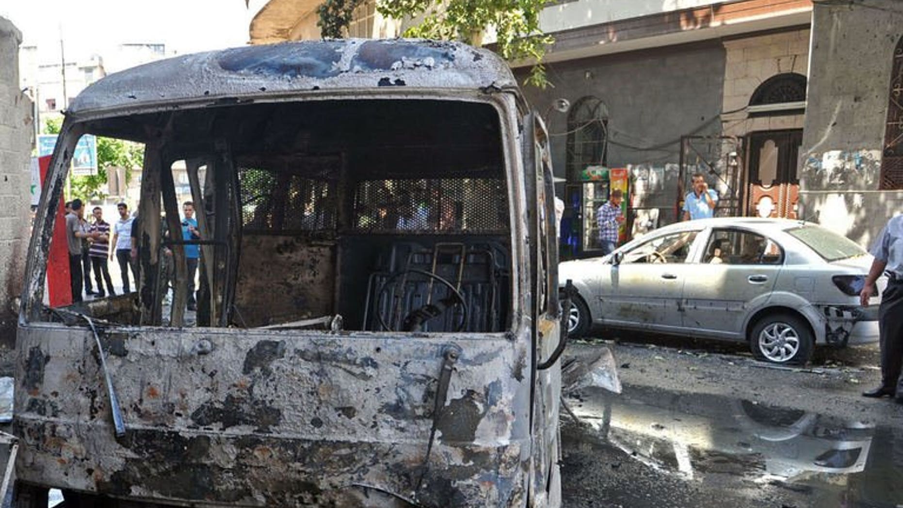 A handout picture released by the Syrian Arab News Agency (SANA) on June 23, 2013, shows civilians inspecting burnt out vehicles following an attack in the capital Damascus.