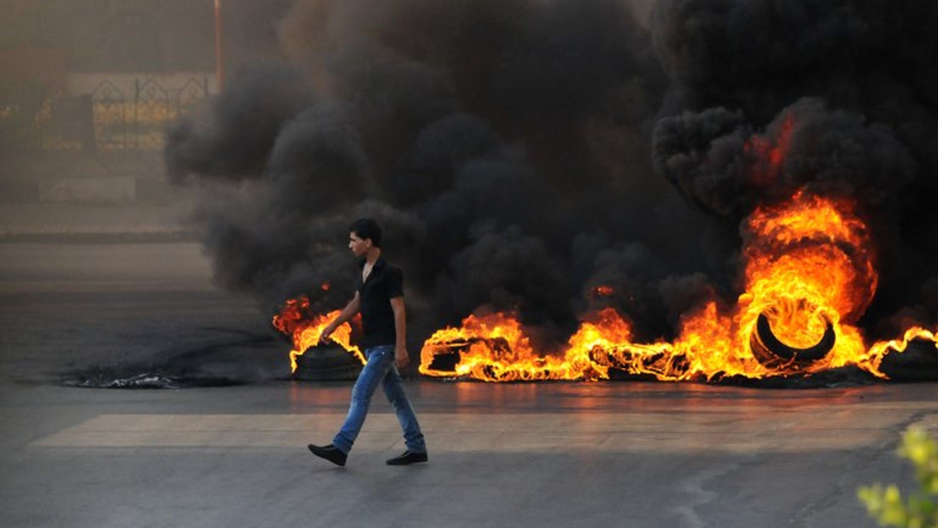 A youth walks past burning tyres in the northern Lebanese city of Tripoli on June 23, 2013 during protests in support of Sunni cleric Sheikh Ahmad al-Assir. At least 12 soldiers have been killed in less than 24 hours of clashes with Assir supporters in Sidon.