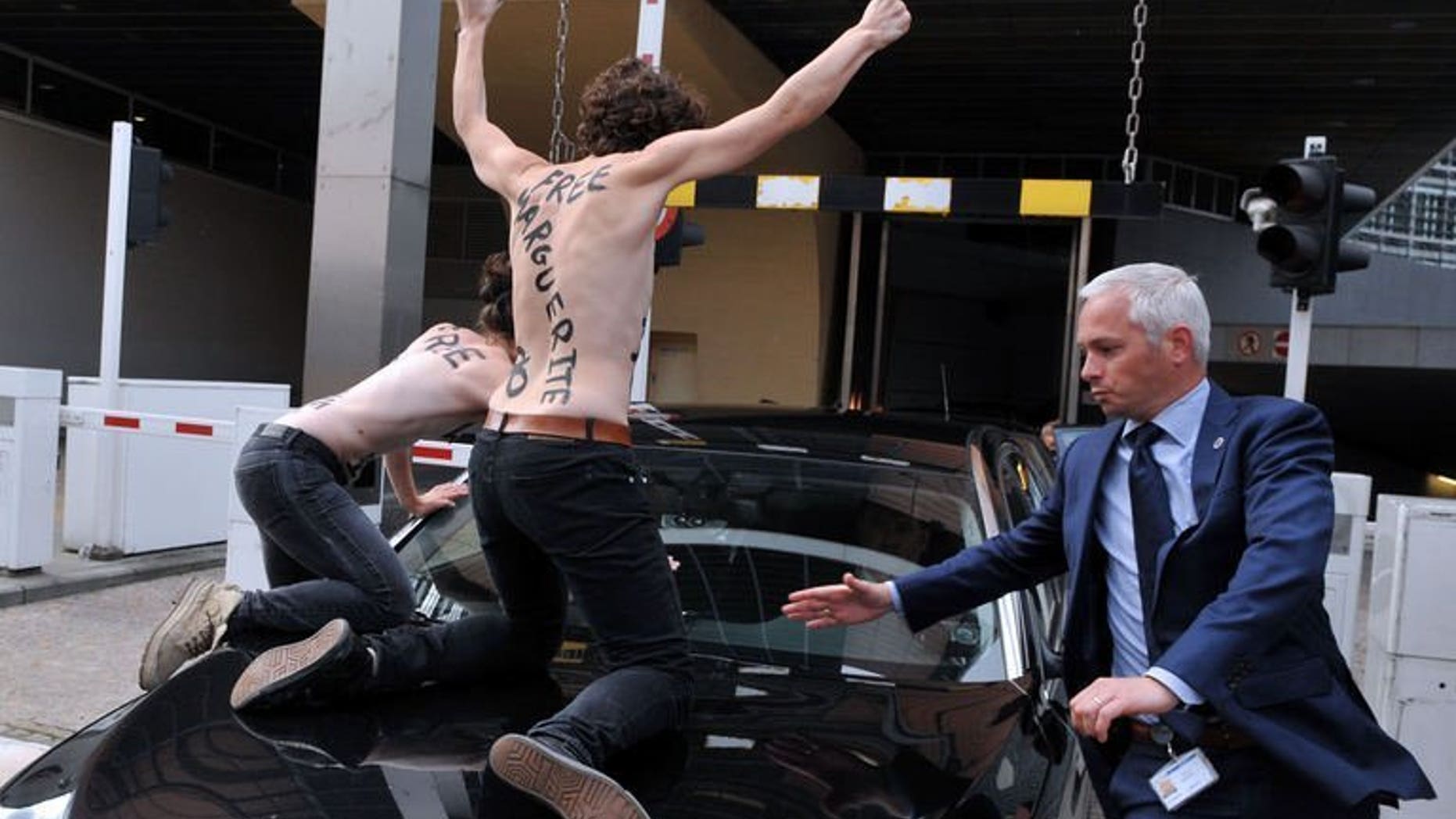 Femen activists try to stop the car of Tunisian Prime Minister Ali Larayedh from leaving the EU commission building after his working session with European Commission President at the EU headquarters in Brussels on June 25, 2013. Three topless feminist activists staged a protest by jumping on the car.