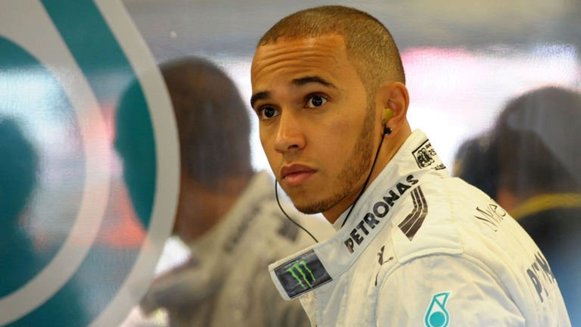 Mercedes' British driver Lewis Hamilton is reflected on a team logo in the pits during the first practice session at the Silverstone circuit on June 28, 2013. The Briton will start from pole position in British Grand Prix.