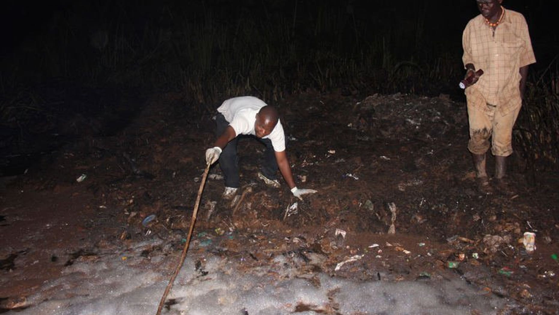 A man uses a stick to as he tries to pull out a body from a hole on June 30, 2013 in Namungoona, a Kampala suburb. At least 31 people have died in a blaze that engulfed an oil tanker after it was hit by another vehicle in a suburb of the Ugandan capital, police said Sunday.