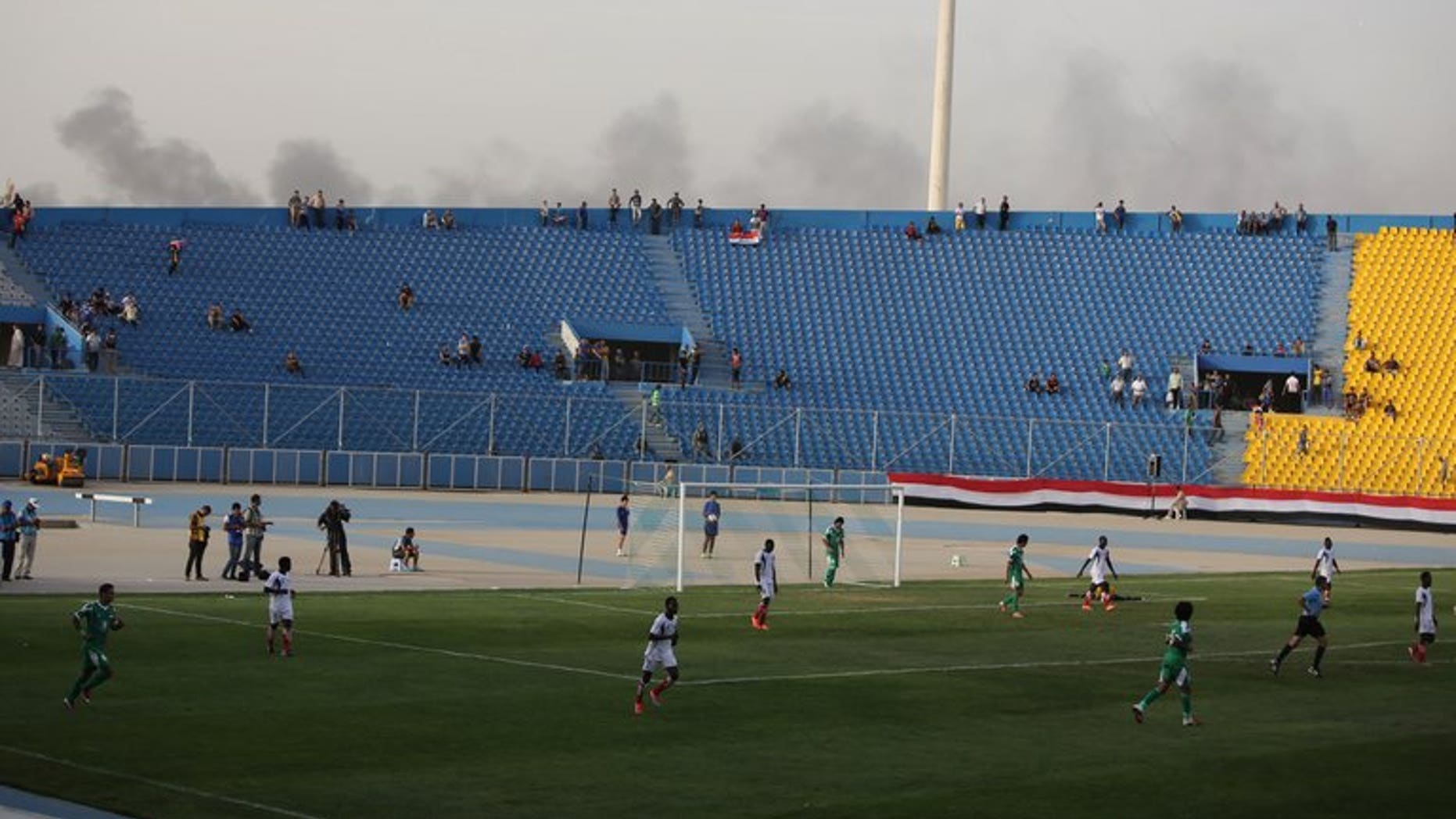 Smoke from explosions billow on the background as Iraq plays a friendly match against Liberia at al-Shaab Stadium in Baghdad on May 27, 2013. FIFA on Wednesday barred Iraq from hosting international football friendlies due to a massive surge in nationwide violence, barely three months after world football's governing body gave Baghdad the go-ahead.