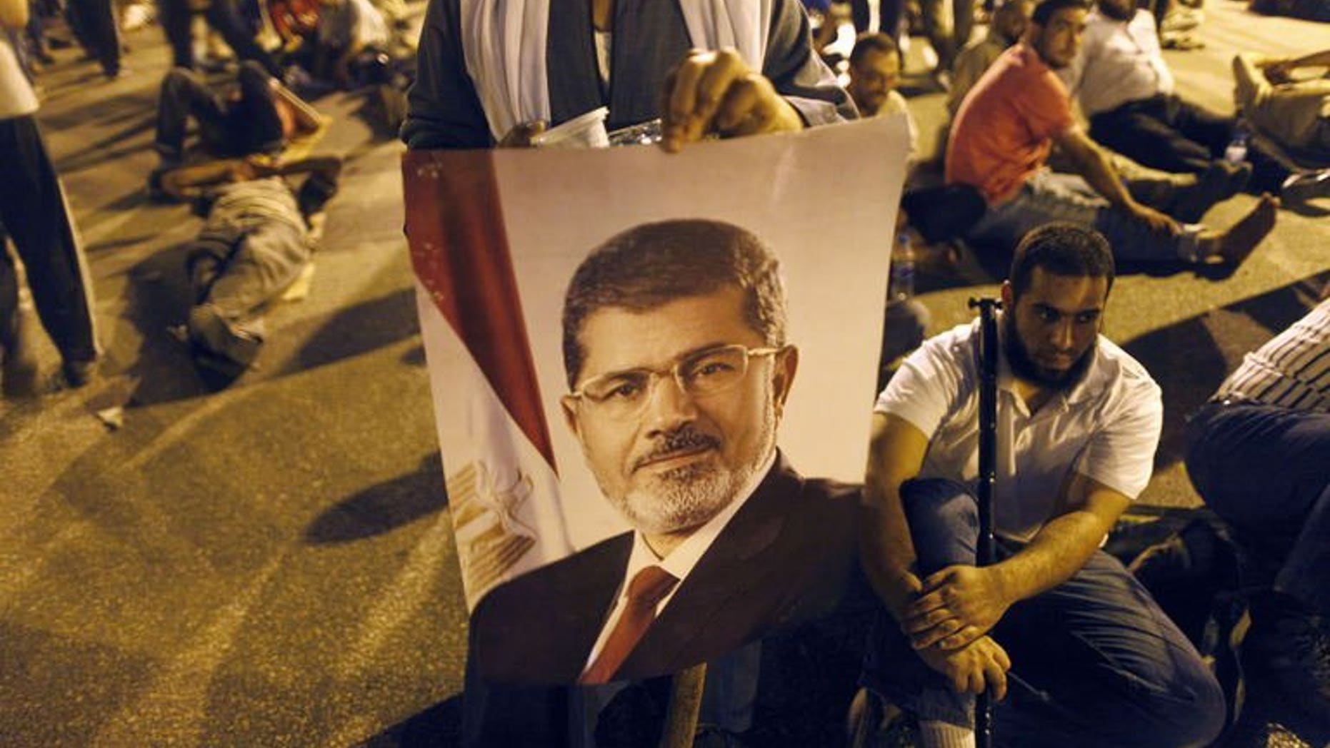 A supporter of the Muslim Brotherhood holds the portraits of deposed president Mohamed Morsi during a rally outside Cairo's Rabaa al-Adawiya mosque late on July 7, 2013. Egypt's prosecution ordered the closure of the Cairo headquarters of the Muslim Brotherhood's Freedom and Justice Party after police found weapons inside it on Monday, a security official said.