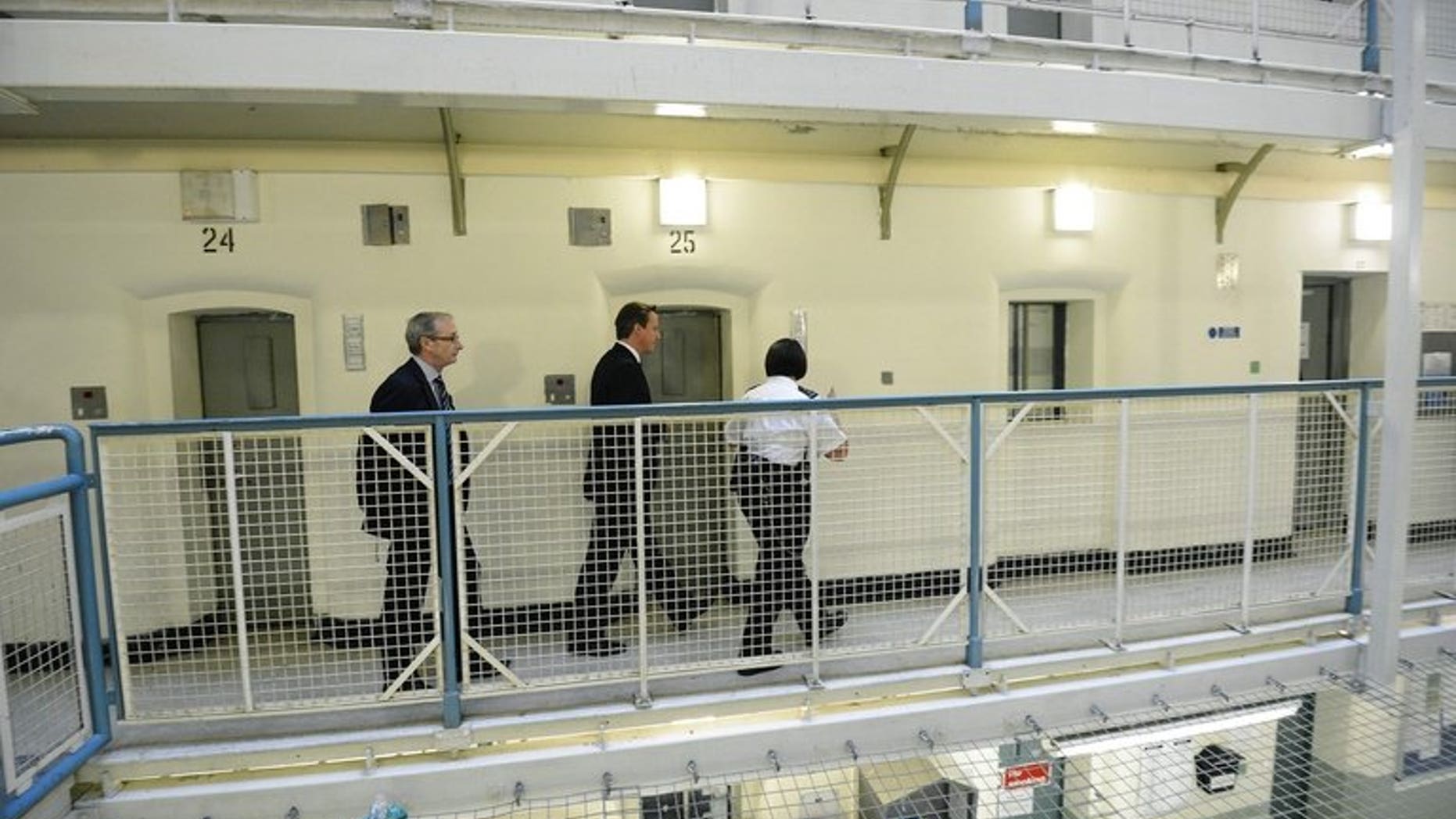Britain's Prime Minister David Cameron (centre) is escorted around Wormwood Scrubs prison in west London on October 22, 2012. Britain's government on Monday pledged to jail bankers found guilty of reckless misconduct, backing a recommendation contained in a report written by a panel of cross-party lawmakers.