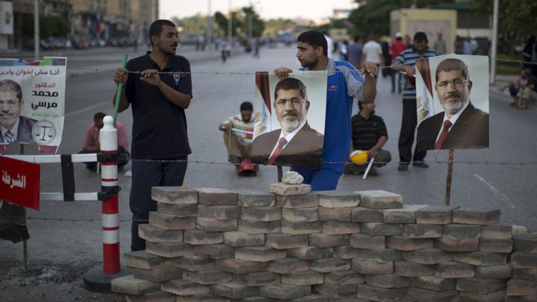 Men hang portraits of Mohamed Morsi on a barricade in Cairo on July 7. Egypt's ousted president is in a "safe place" following his overthrow by the military, a foreign ministry spokesman told reporters on Wednesday, adding that no charges had been levelled against him yet.