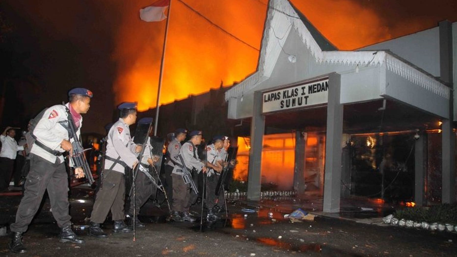 Indonesian policemen secure the entrance of a burning prison compound in Medan city on July 11, 2013. At least five people have been killed in violent riots at the jail and about 100 prisoners, including terror convicts, are still on the loose, police said Friday.