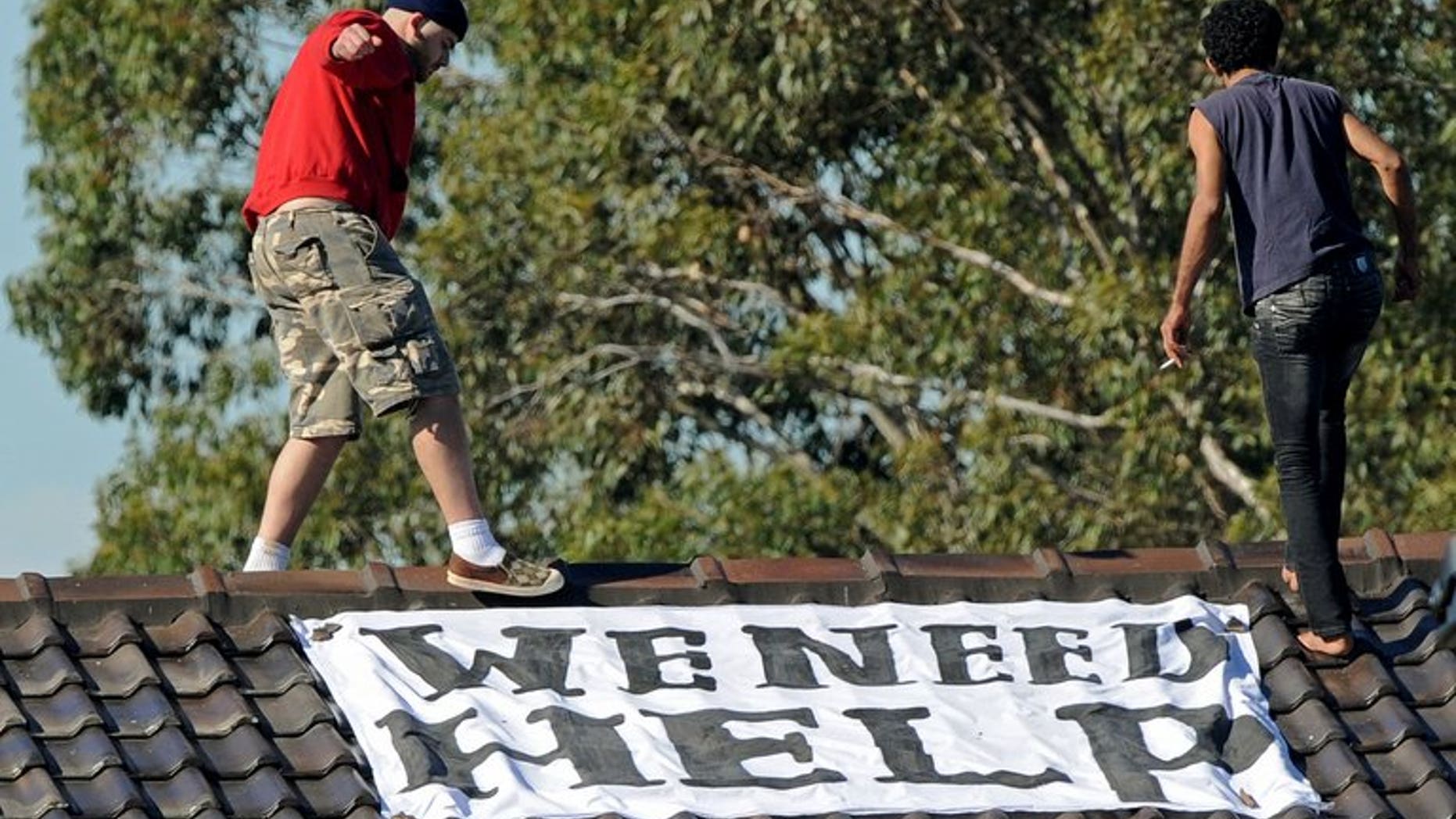 Asylum seekers (top) walk past a banner on top of a building at Sydney's Villawood Detention Centre on April 21, 2011. The UN refugee agency on Friday criticised conditions at a detention centre in Papua New Guinea where Australia sends asylum-seekers, wading into an issue looming large in Australia's forthcoming election.
