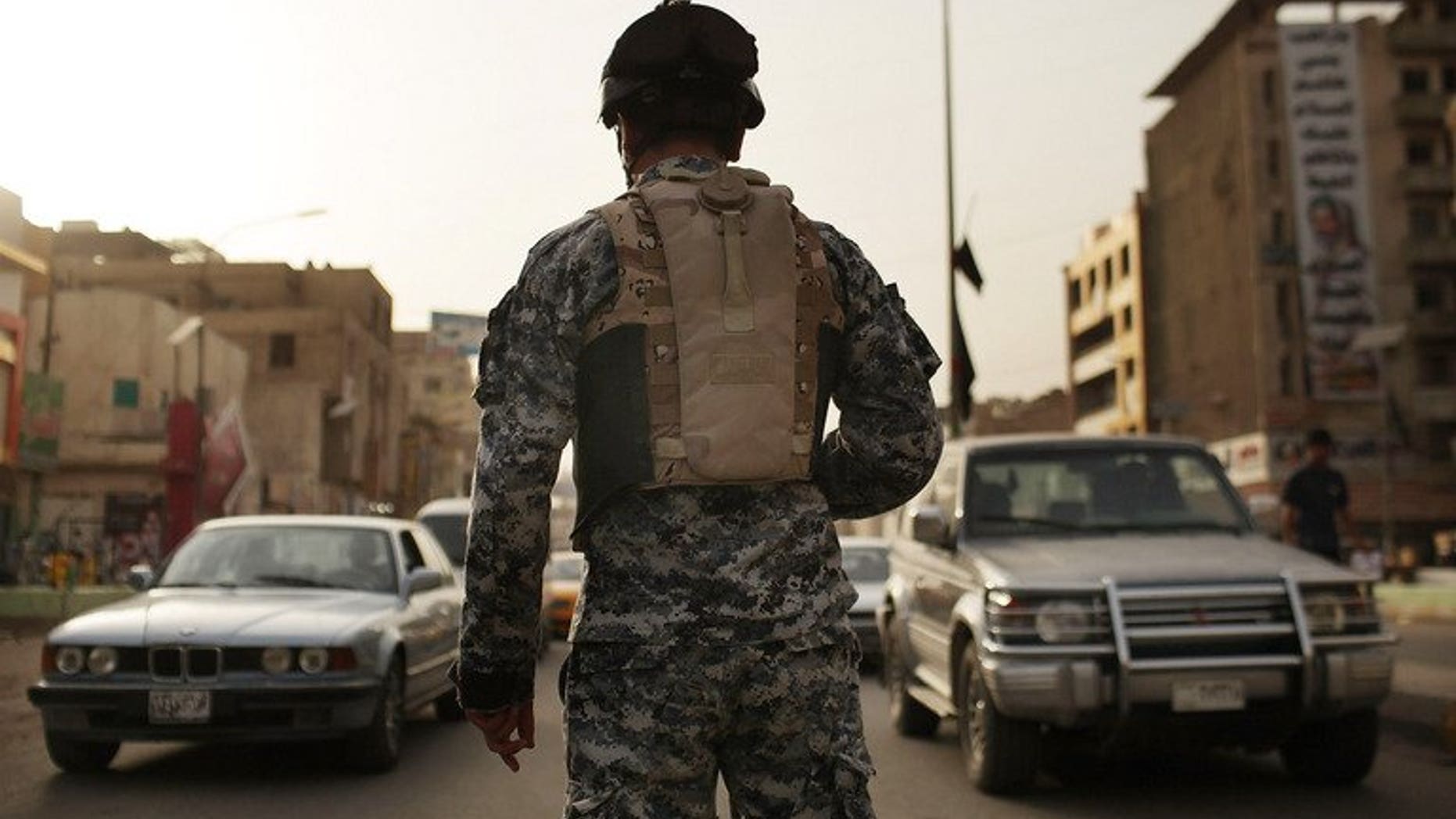 An Iraqi police officer watches cars at a checkpoint on July 20, 2011 in Baghdad. A British soldier accused of overcharging a US peace group for a security contract with the private firm he set up will be extradited to the United States, the Home Office said.