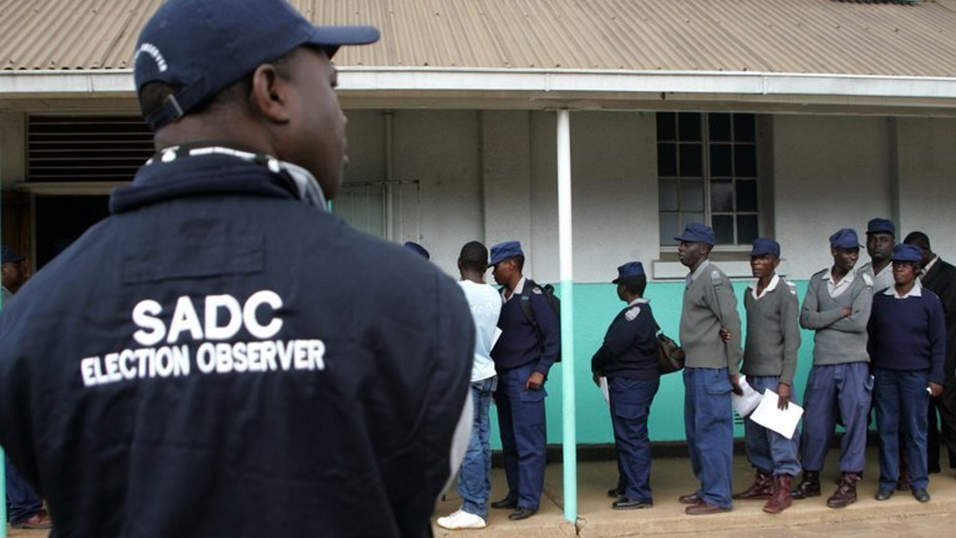 An election observer looks on as Zimbabwe security forces queue to vote in Harare on July 14, 2013. Zimbabwean security personnel unable to cast their ballots during chaotic early polling this week will get another chance to vote on July 31, the country's elections chief has announced.