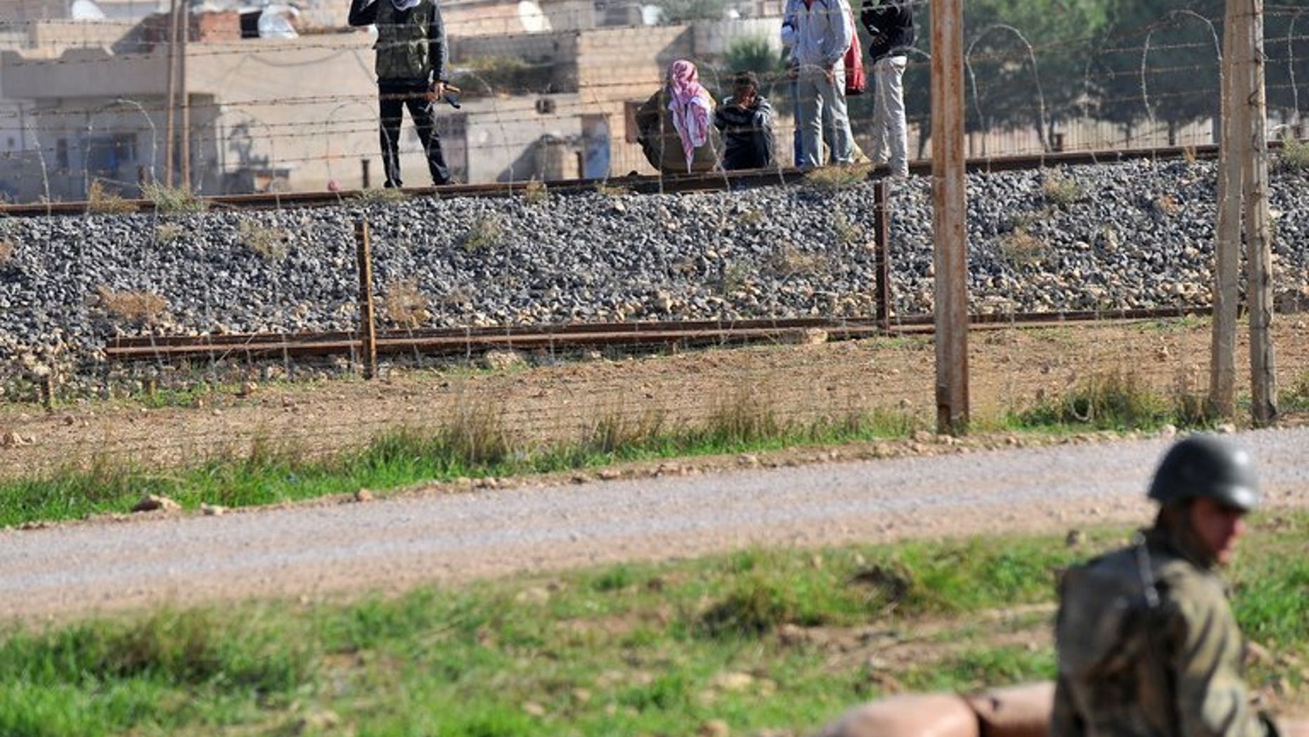 A Turkish soldier (R) in a foxhole in the southeastern Turkish border town of Ceylanpinar watches Syrian opposition fighters in the Syrian border town of Ras al-Ain on November 15, 2012. A 17-year-old died of his injuries in Ceylanpinar on Wednesday after he was hit by stray gunfire coming across the border from war-torn Syria, local media reported.