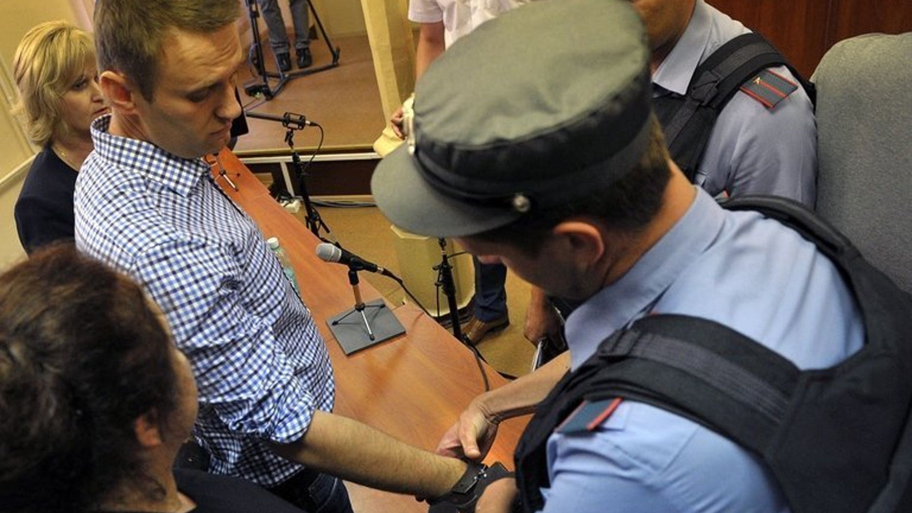 A police officer handcuffs Russian opposition leader Alexei Navalny (L) in the courtroom in Kirov, northern Russia on July 18, 2013. Navalny is pulling out of the Moscow mayoral race and is calling on his supporters to boycott the vote, his election chief said Thursday.