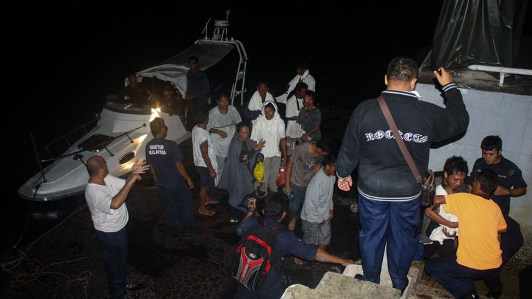 This photo, released by the Malaysian Maritime Enforcement Agency on July 18, 2013, shows passengers who were rescued from an overturned boat near Tanjung Sedili, Johor, southern Malaysia. An Indonesian woman died and seven other people remain missing after a wooden boat, believed to be smuggling them out of Malaysia, overturned.