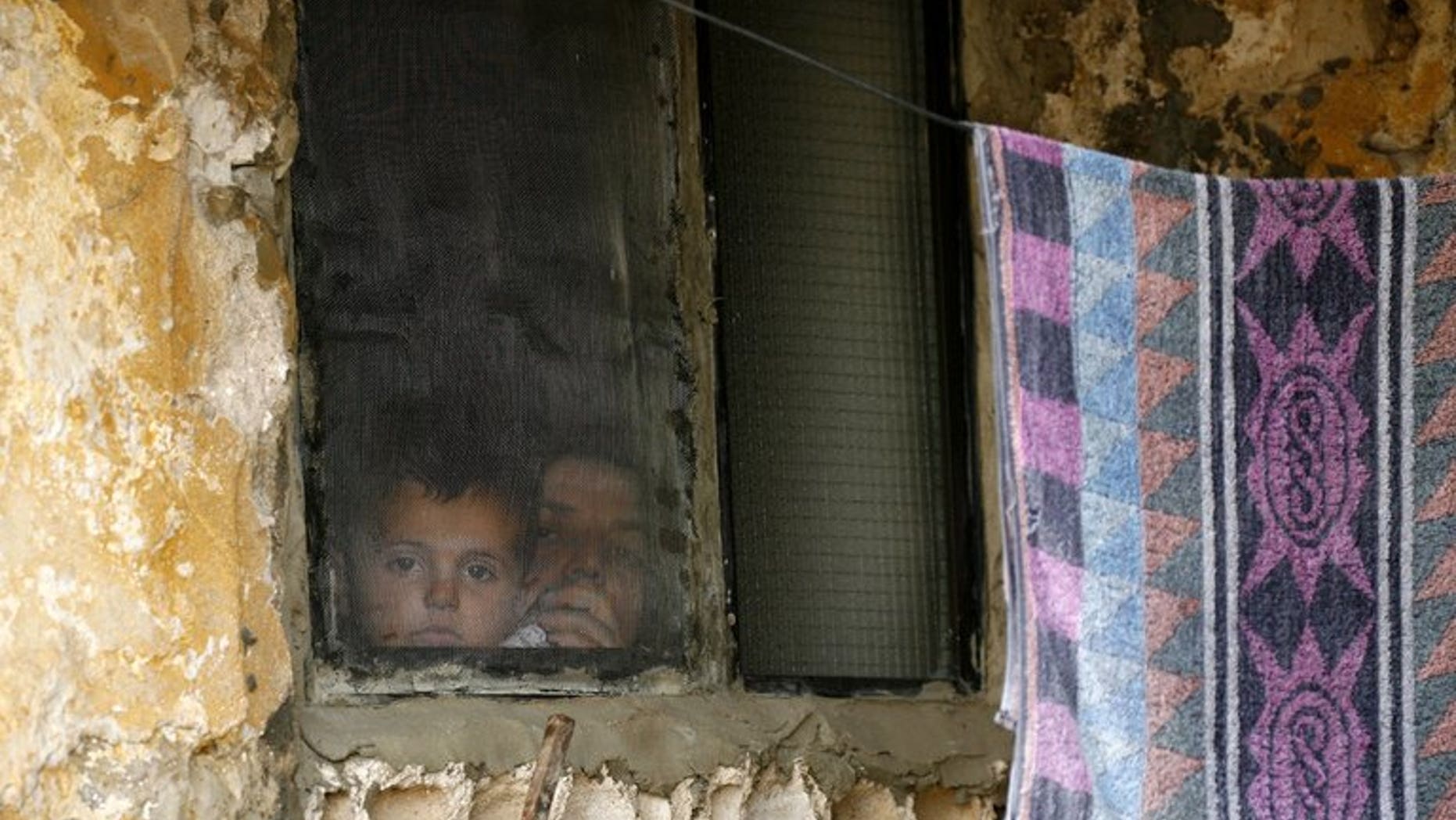 A Syrian woman and her child look out of a window at a refugee camp in the Lebanese town of Alman on June 20, 2013. Two Syrian refugee children in Lebanon suffocated to death overnight in a fire started by a lit candle during a power outage, Lebanon's state news agency reported on Friday.