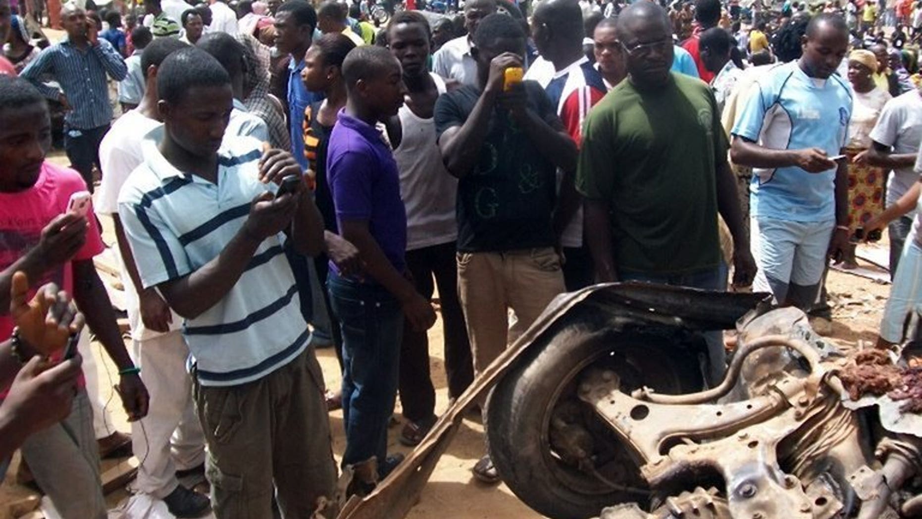 People take photographs with their mobile phones of a destroyed car used in a suicide bombing in Jos, on June 10, 2012. Mobile phone service have returned to the restive Nigerian city of Maiduguri for the first time in more than two months, the latest area of the conflict-torn northeast to be reconnected.