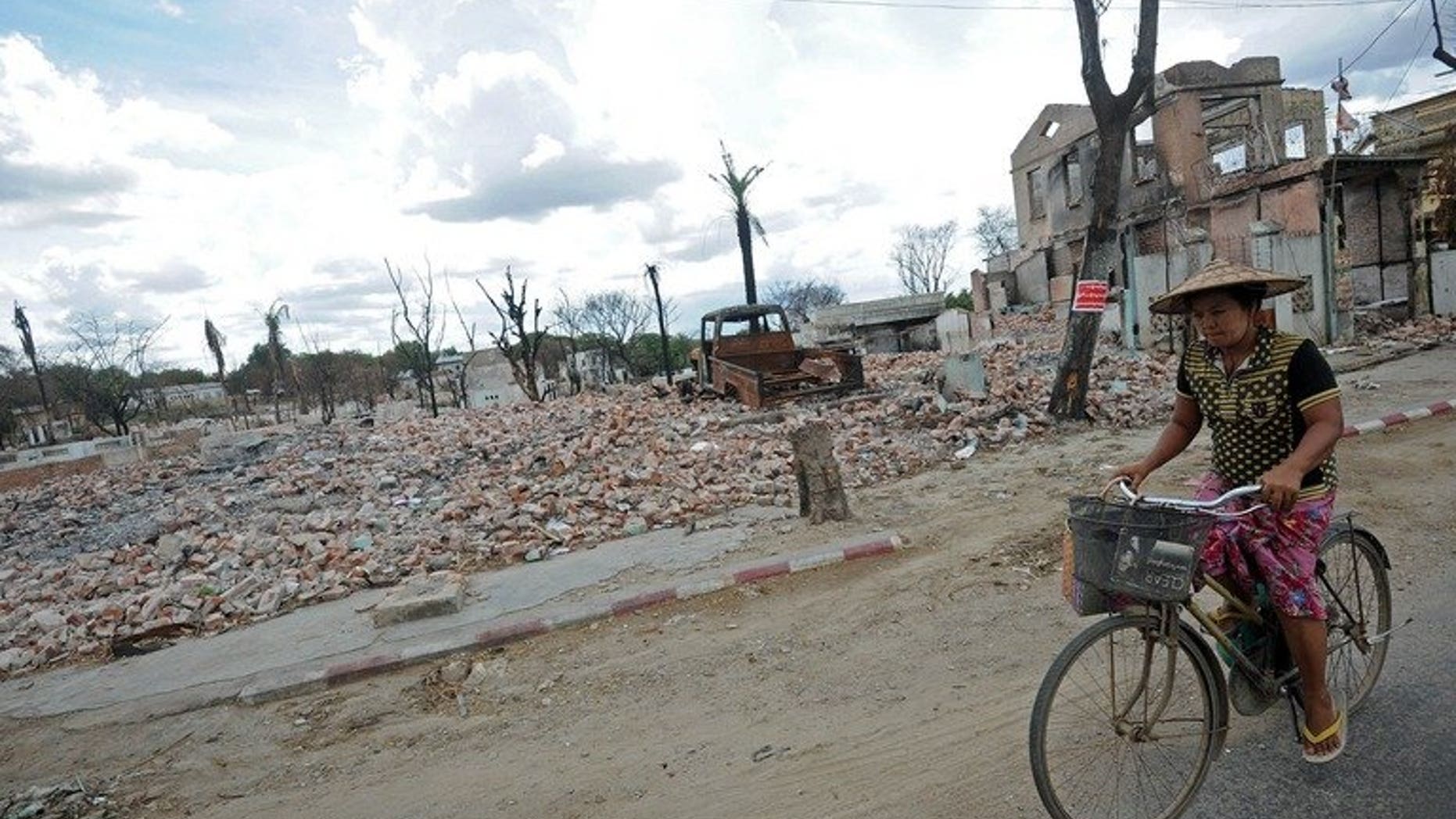 A local resident is seen riding her bicycle past the ruins of destroyed buildings in riot-hit Meiktila, central Myanmar, on June 4, 2013. Myanmar has lifted a state of emergency imposed in the riot-hit area in March where dozens of people were killed in religious violence.