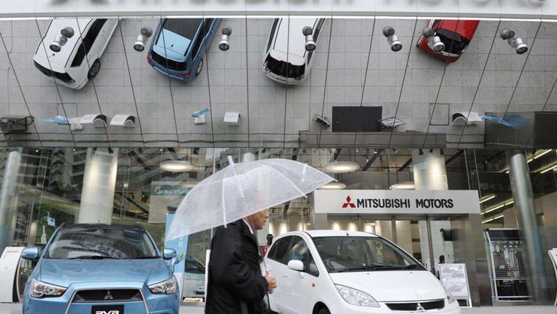 A man holding an umbrella walks past a showroom of Mitsubishi Motors Corp. in Tokyo on April 27, 2010. Mitsubishi Motors recalled more than 650,000 small cars sold in Japan over a possible fire risk.