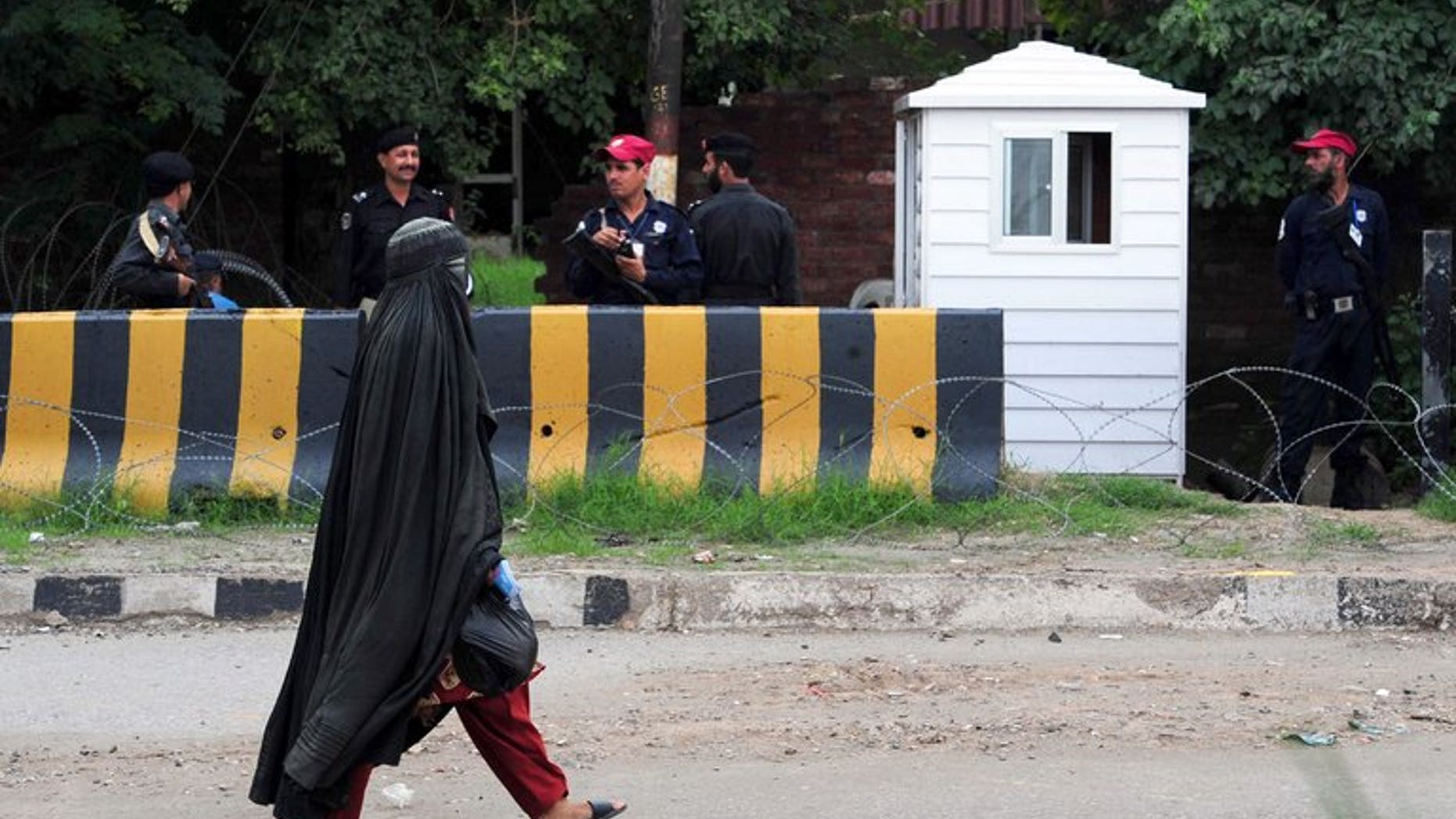 A veiled woman walks past Pakistani security personnel in Peshawar on September 17, 2012. A new cartoon superhero disguised in a flowing black burka is set to debut on Pakistani television next month in an animated series which follows her battle for girls' education in Pakistan.