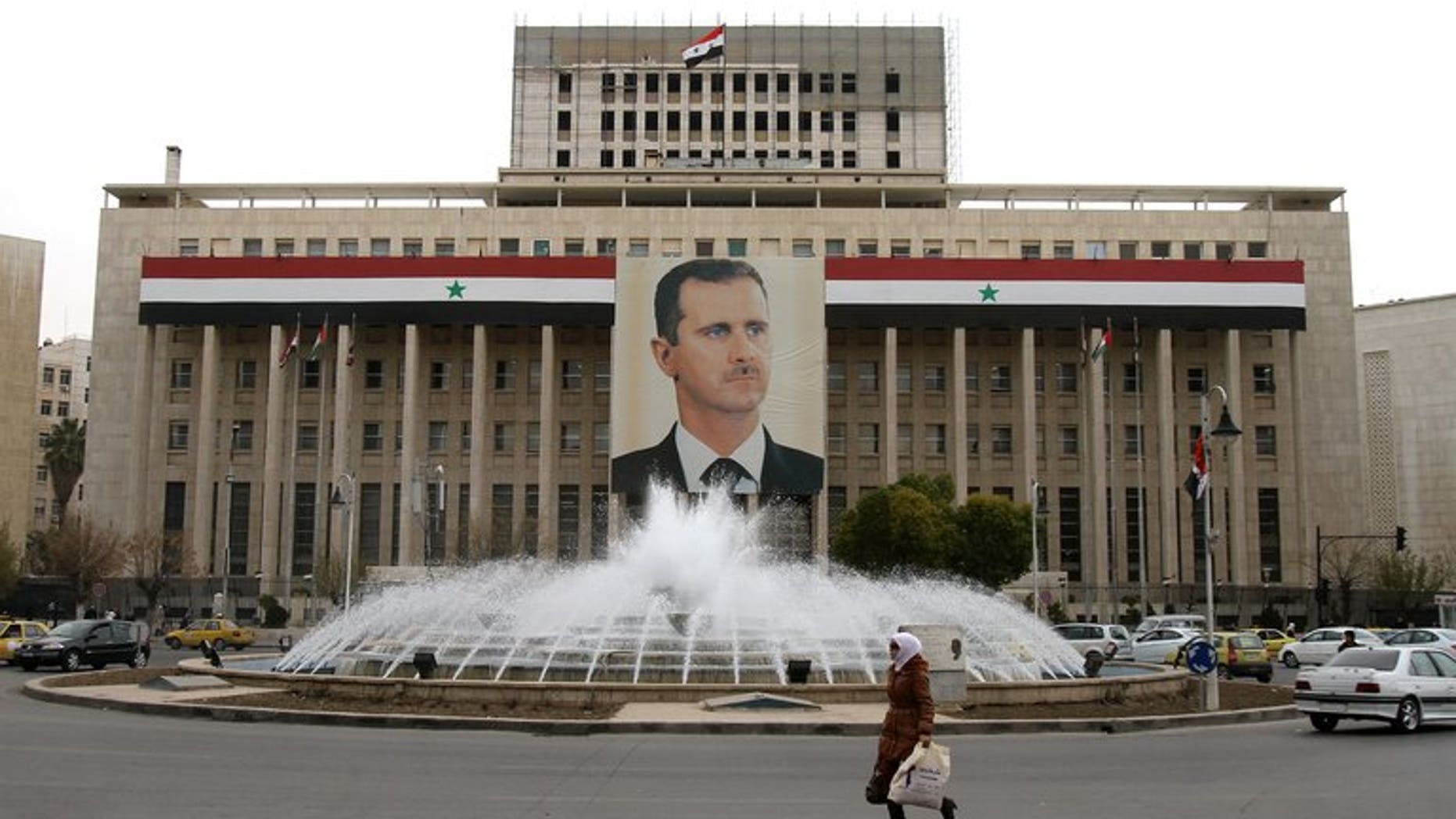 A woman walks past the central bank building decorated with a huge banner of President Bashar al-Assad in the capital in Damascus on February 28, 2012. Iran has agreed to supply Damascus with $3.6 billion in oil in exchange for the right to invest in the country, Syria's state news agency SANA said on Tuesday.