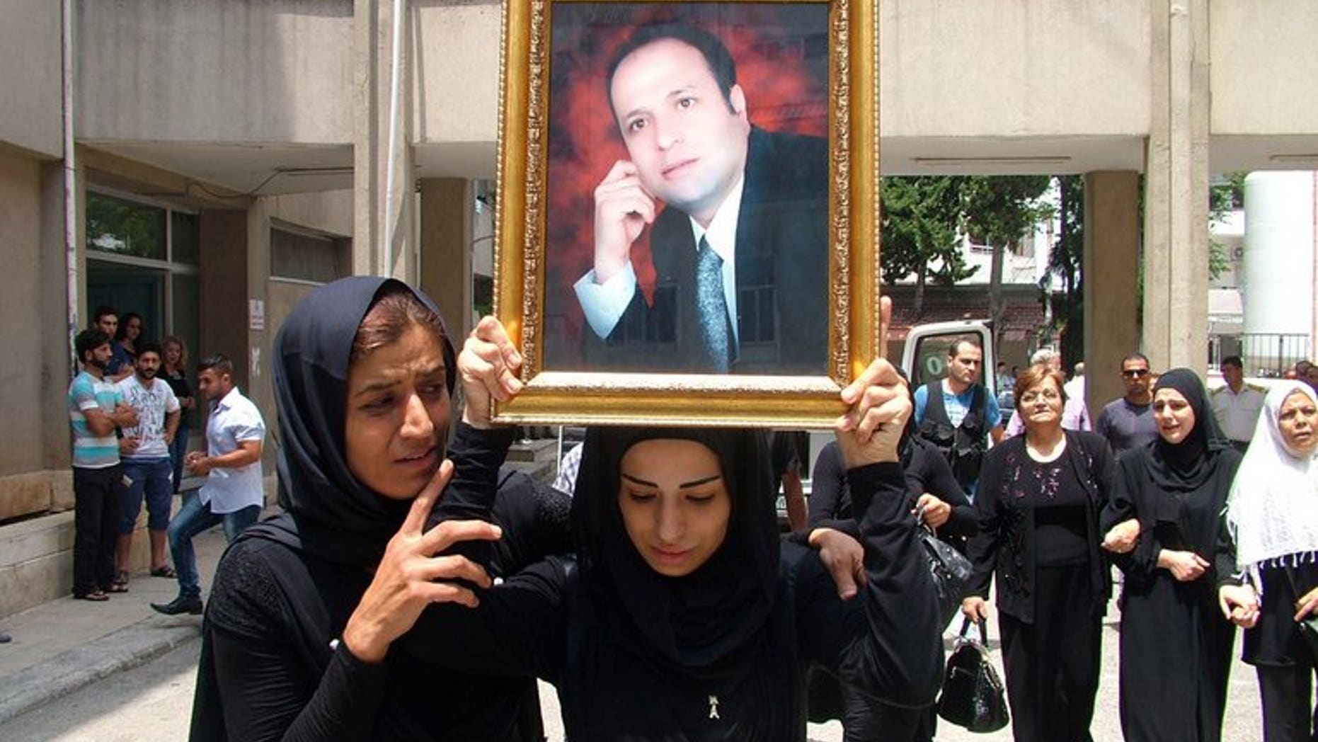 The daughter of Mohammad Darrar Jamo carries his portrait during his funeral in the Latakia province on July 19, 2013. The wife of the slain Syrian political analyst and ardent supporter of President Bashar al-Assad was charged in Lebanon on Wednesday with incitement to murder.
