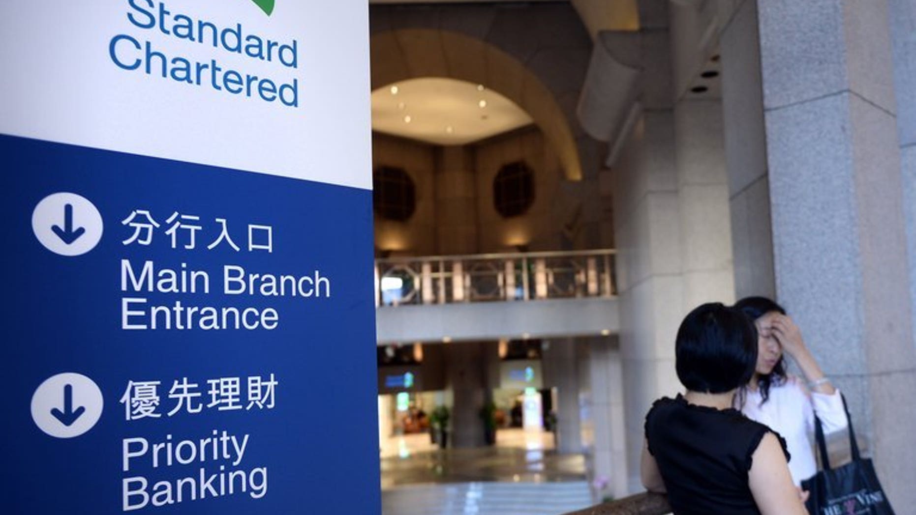 Two women inside a Standard Chartered bank branch in Hong Kong Tuesday. Standard Chartered on Tuesday said its first-half net profit fell 24 percent, with some of its businesses in emerging Asian markets seeing slower growth.