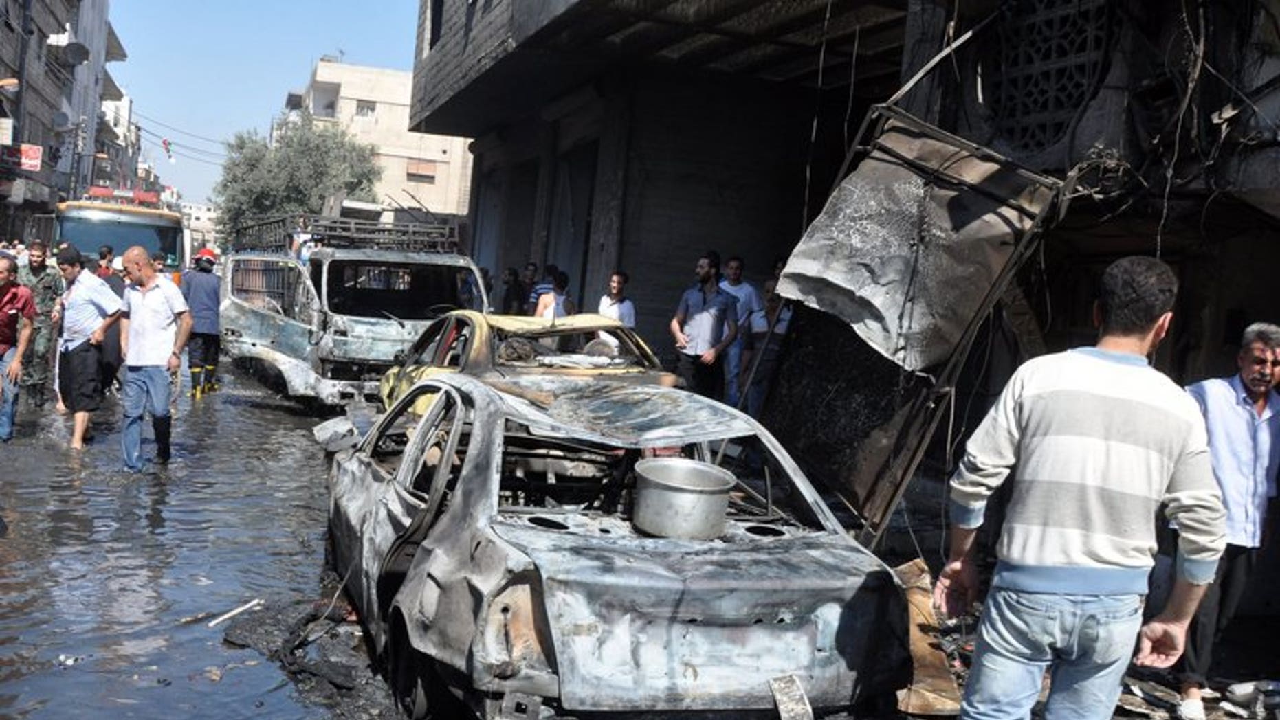 Syrians walk past a burned-out car after an attack on July 25, 2013 in the Jaramana suburb in southeast Damascus. A bomb killed 10 people in Jaramana on Tuesday, the latest in spate of blasts to hit the mainly Christian and Druze district, state television said.
