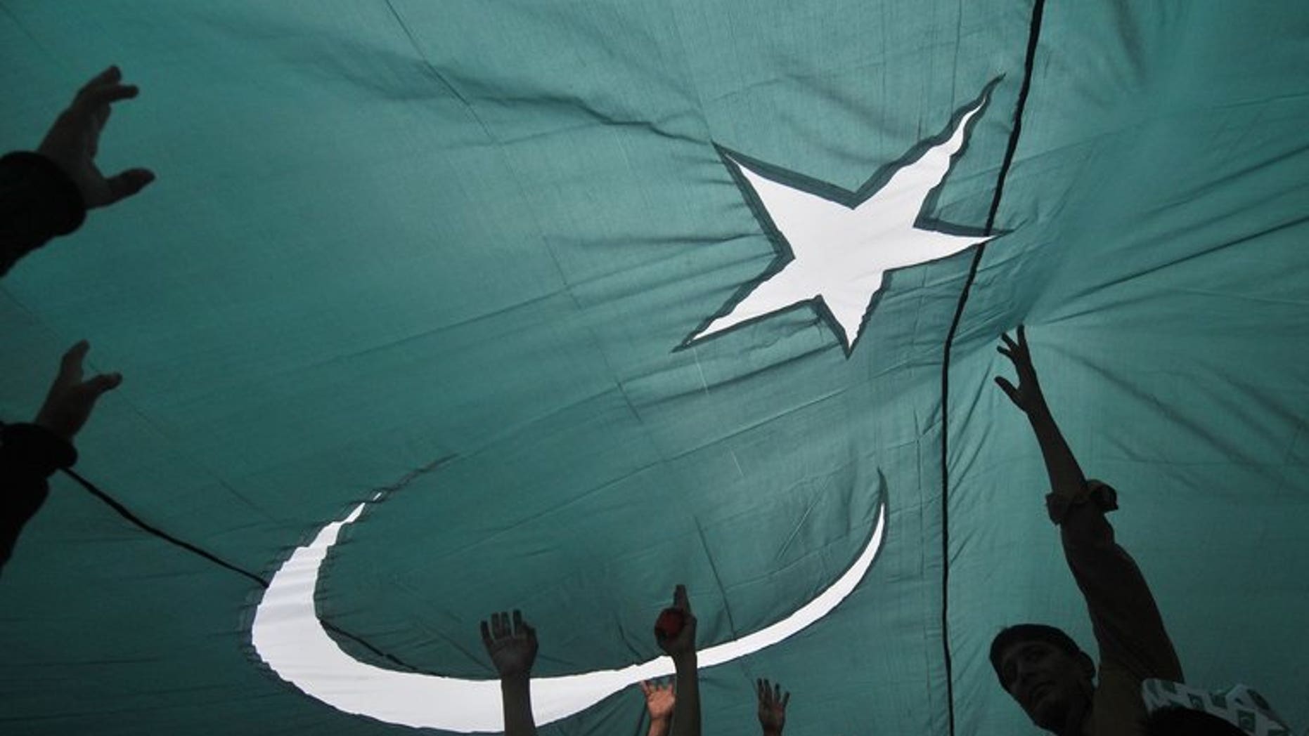 Youths gather under a giant national flag in Lahore on August 13, 2013, one day ahead of the country's Independence Day. At least one person was killed and more than 30 wounded in Karachi on Wednesday as hundreds of people fired guns in the air to celebrate Pakistan's Independence Day.