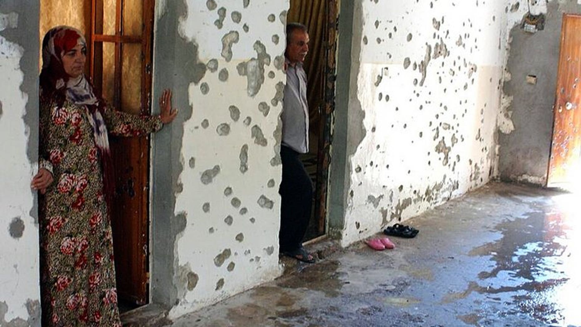 A man and a woman stand next to a wall riddled with bullets in the courtyard of a house in the Syrian town of Ras al-Ain on August 3, 2013. Al-Qaeda loyalists attacked a mainly Kurdish town in northeastern Syria sparking fighting in which 17 people were killed, two of them ambulance crew, a watchdog said on Saturday.