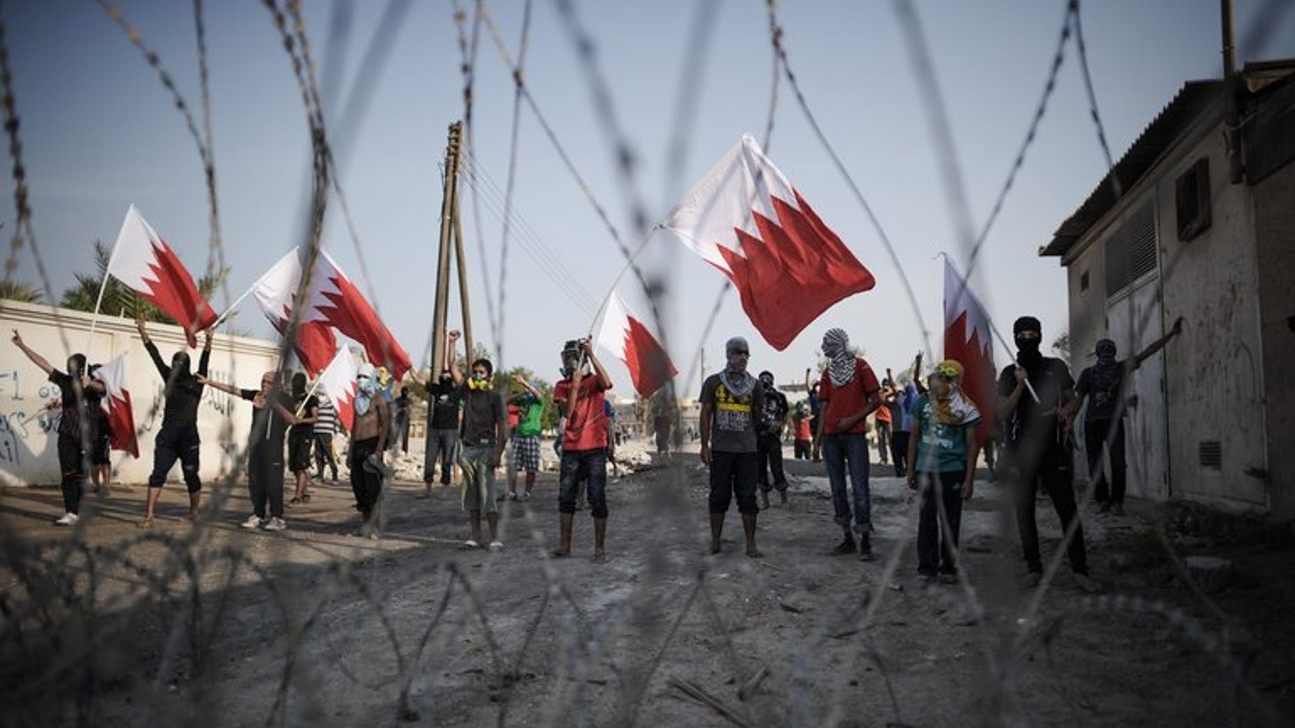 Bahraini protestors wave their national flag as they stand behind barbed wire placed by riot police during demonstration against the ruling regime in the village of Shakhora, west of Manama, on August 14, 2013. Five Bahraini police were wounded late on Saturday, as security forces clashed with opposition protesters in a Shiite village north of the capital, police said.