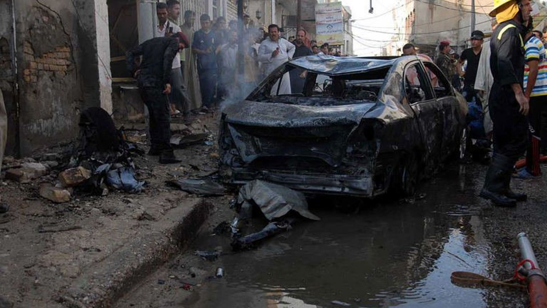 Iraqis gather near the remains of a vehicle at the scene of a car bomb in Nasiriyah, south of Baghdad on August 19, 2013. Attacks in Iraq killed seven people, damaged an oil pipeline and hit a Shiite shrine on Wednesday, as the country grapples with a months-long spike in violence.