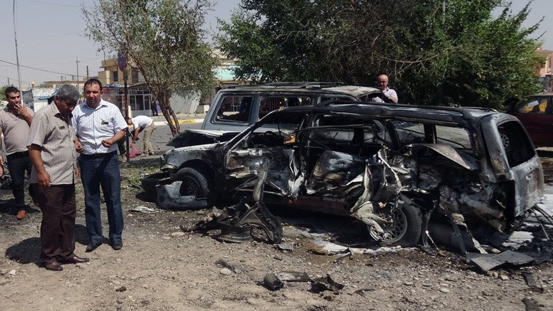 Iraqi investigators talk near a damaged vehicle after a car bomb exploded outside the ministry of education in the northern Iraqi city of Kirkuk on August 22, 2013. Gunmen killed five people, including two soldiers, in Iraq on Thursday, officials said, the latest in a spike in violence that the government has so far failed to stem.