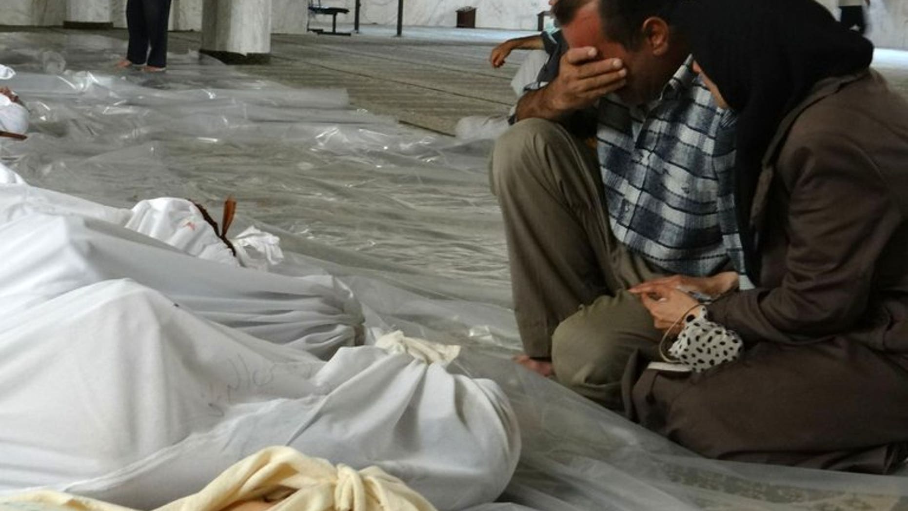 A handout image released by the Syrian opposition's Shaam News Network shows a Syrian couple mourning in front of bodies wrapped in shrouds ahead of funerals following what Syrian rebels claim to be a toxic gas attack by pro-government forces in eastern Ghouta, on the outskirts of Damascus on August 21, 2013.