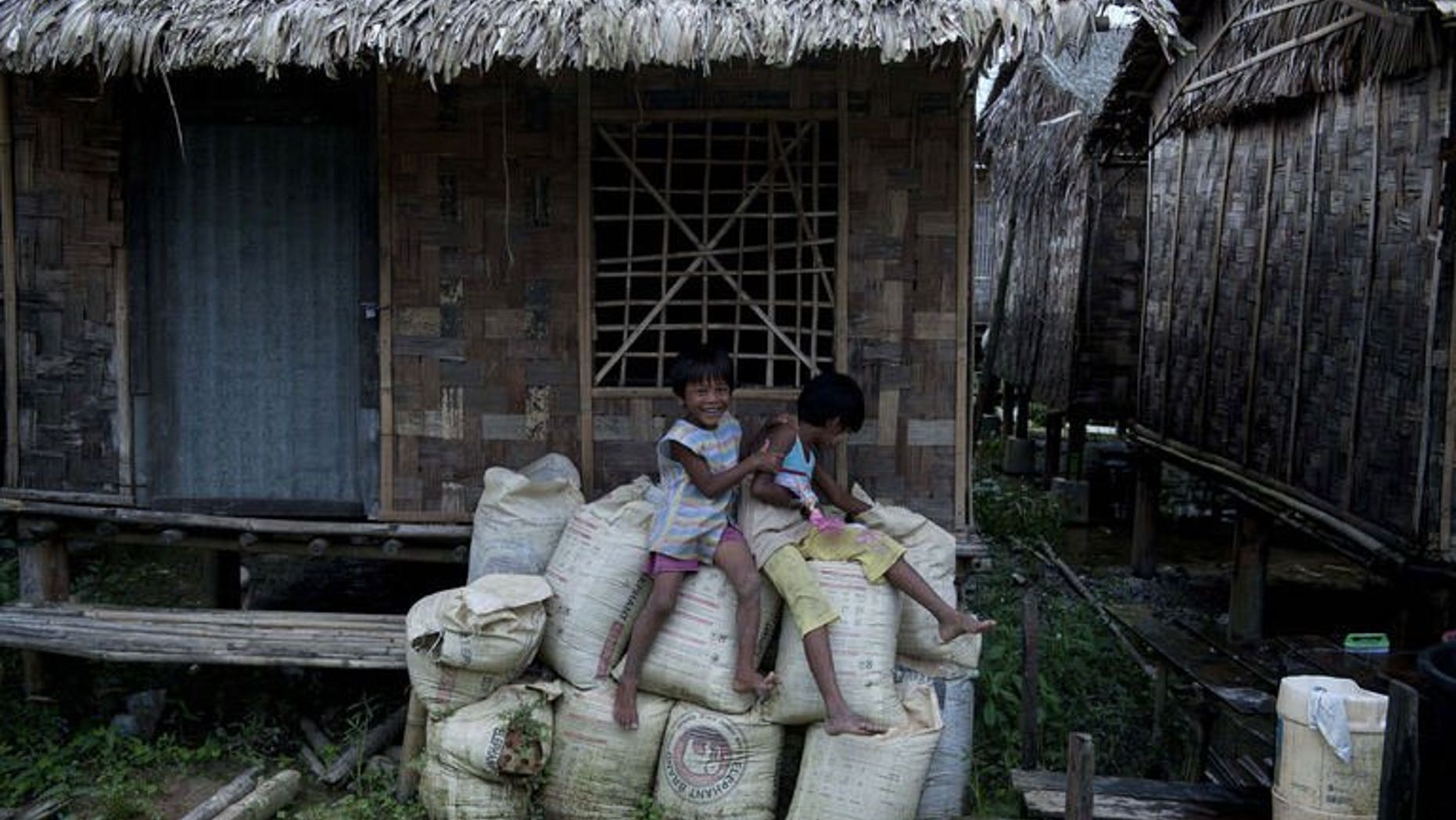 Children sit outside their bamboo house built in the compound of a Buddhist monastery and meditation center sheltering hundreds of displaced families in a suburb of Myanmar's former capital Yangon on July 19, 2013.