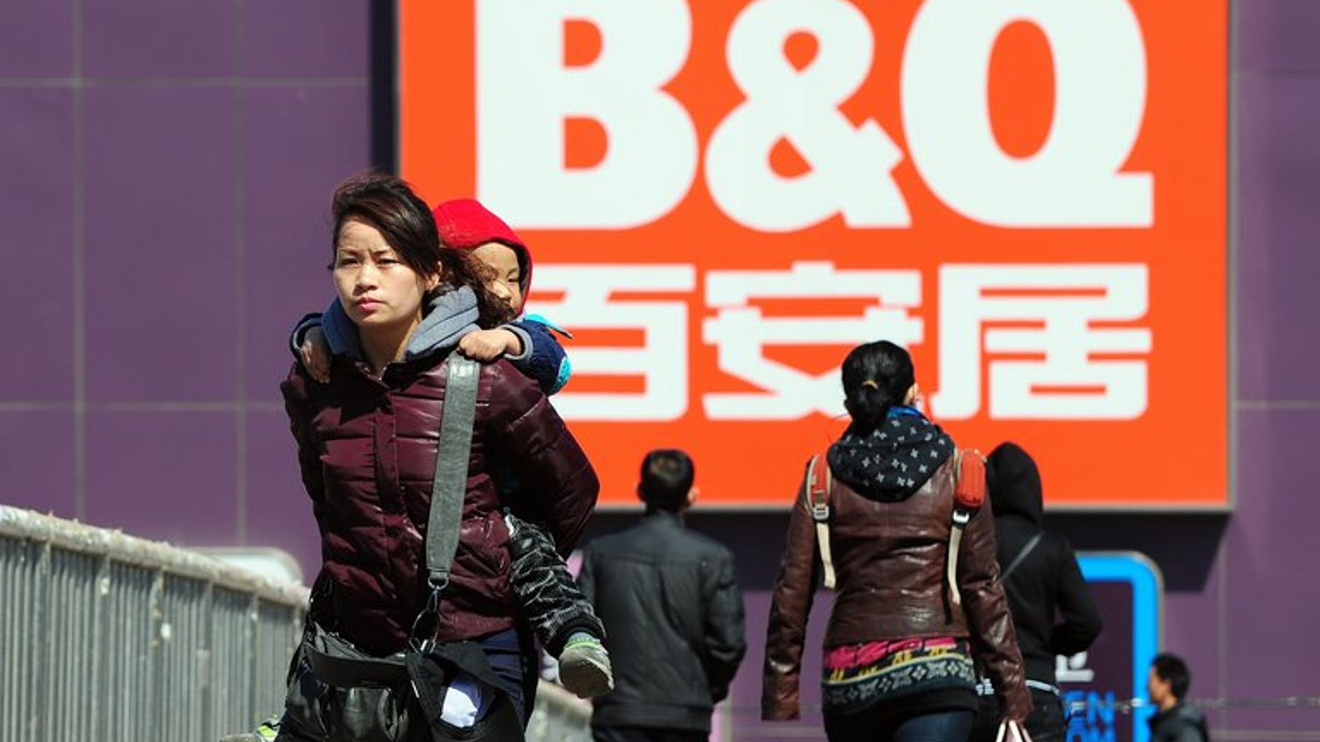 A woman carries a child on her back as pedestrians cross a footbridge overpass in front of a B&Q DIY shop in Beijing on March 24, 2011. Kingfisher, Europe's biggest home-improvements retailer, said that group net profit surged by 70 percent during the first half of its financial year mainly thanks to an exceptional tax gain.