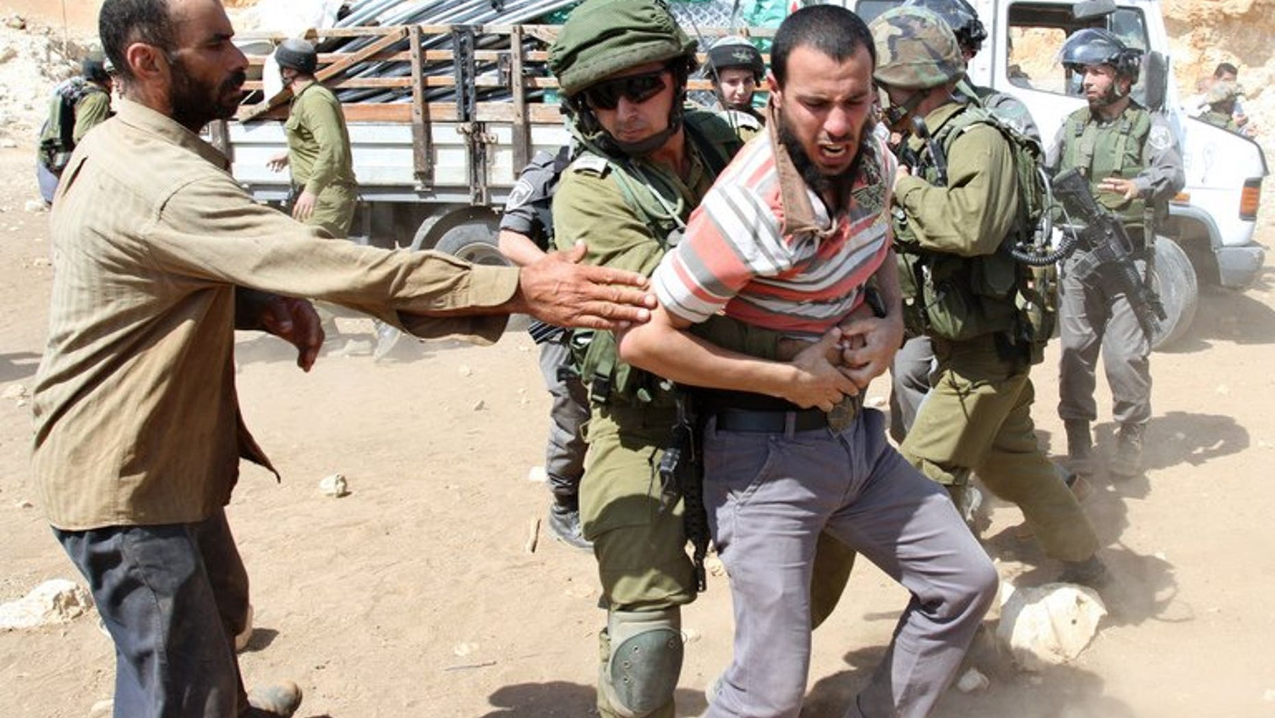 An Israeli soldier restrains a Palestinian man near a truck loaded with supplies on September 20, 2013 on a road leading to the West Bank village of Khirbet al-Makhul.